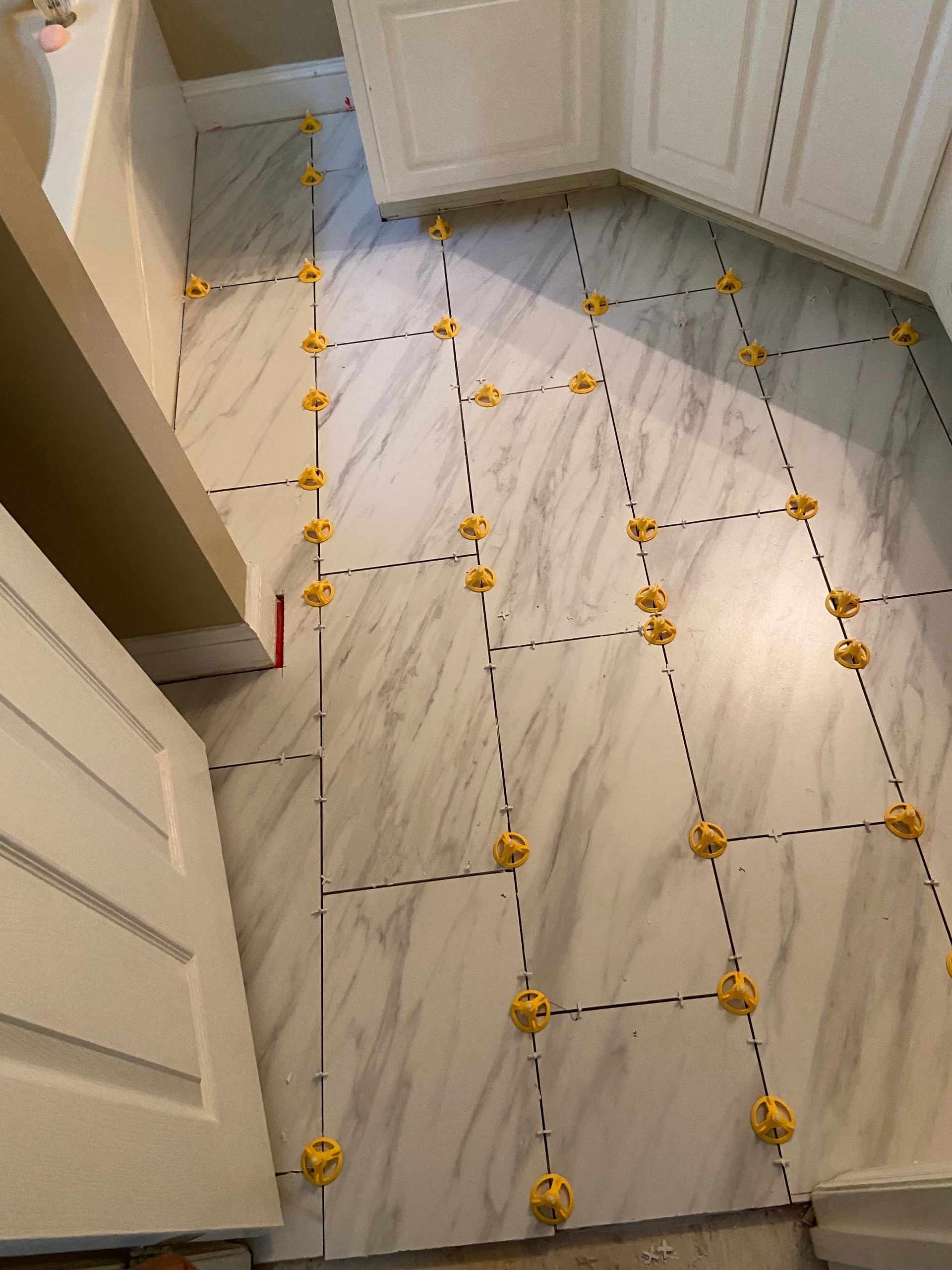 Person installing floor tiles, using a level, trowel, and spacers. Gray cement and beige tiles.