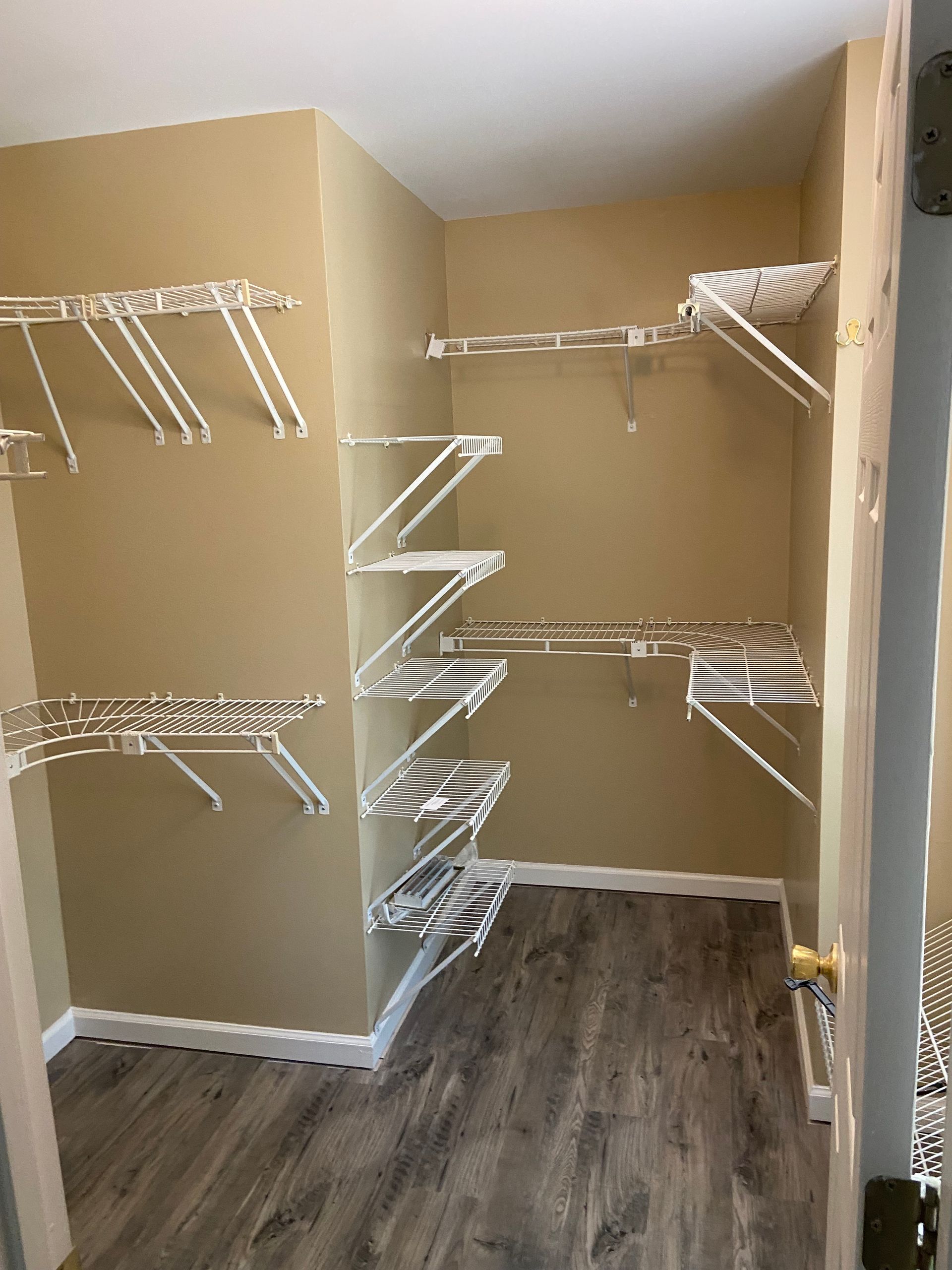 Empty walk-in closet with white wire shelving and a wood-look floor. Beige walls, white trim.