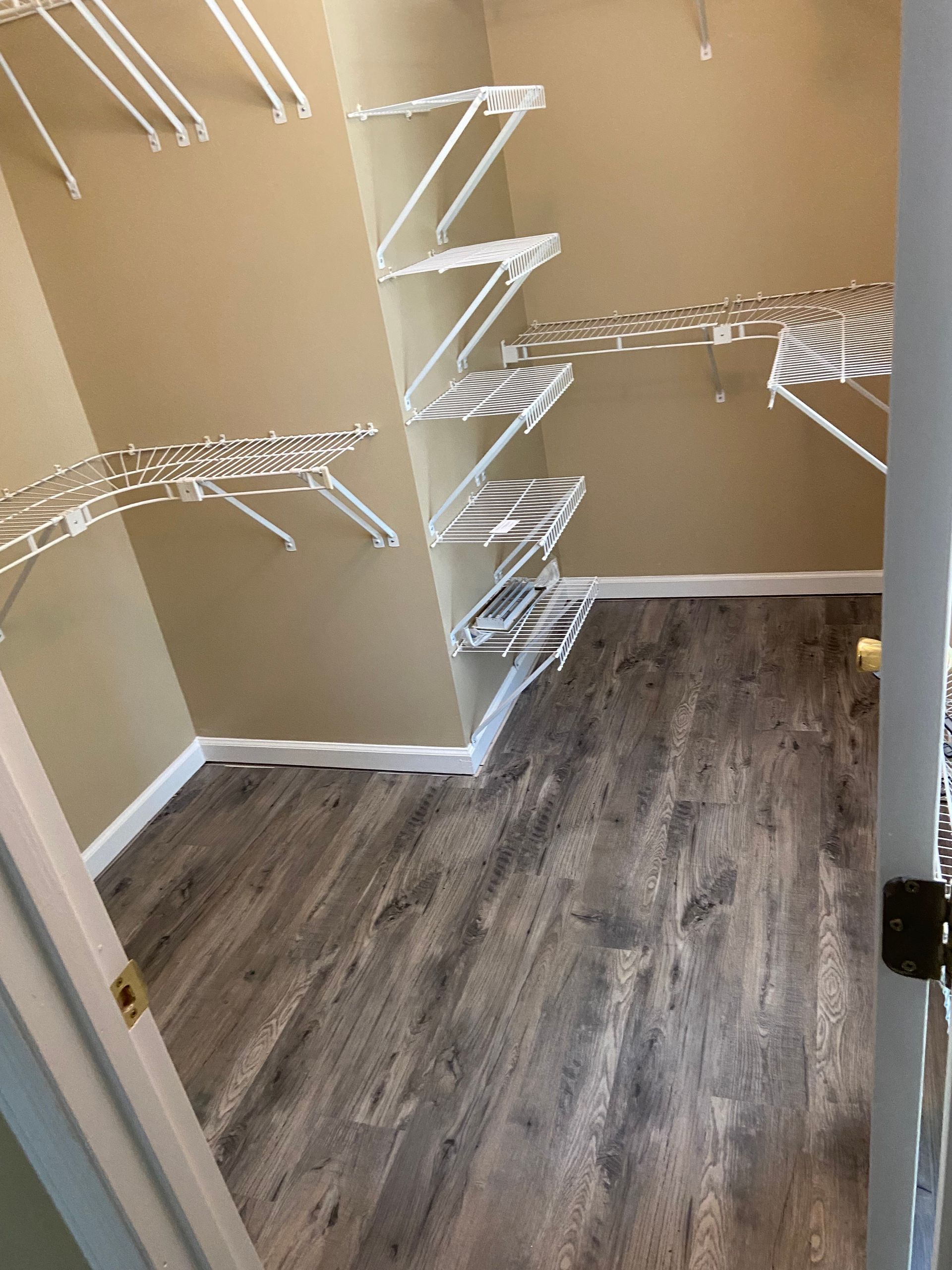 Empty closet with wire shelving and wood-look floor. Beige walls, white trim and shelves.