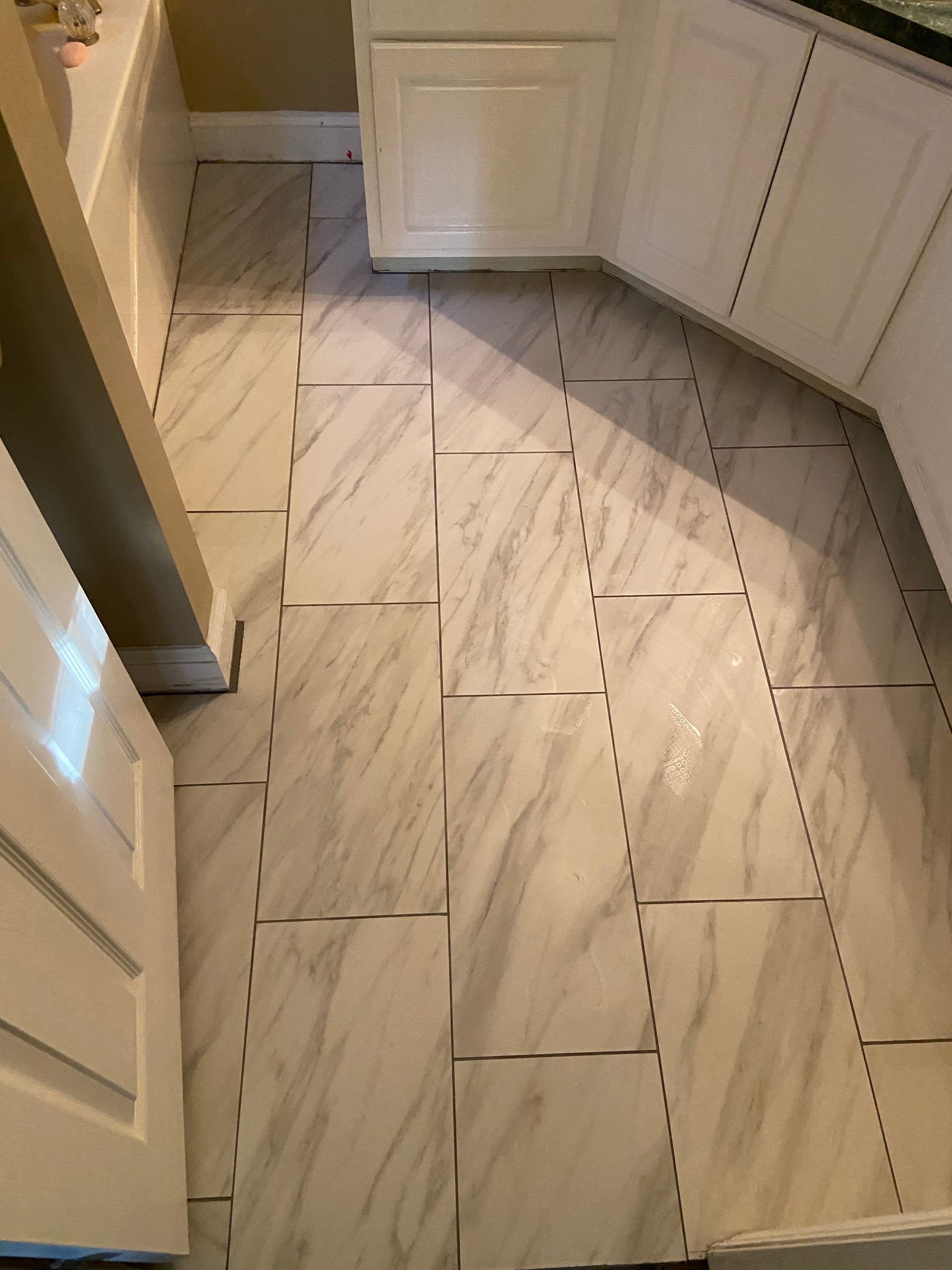 Kitchen floor with light gray marble tiles. Cabinets are white.