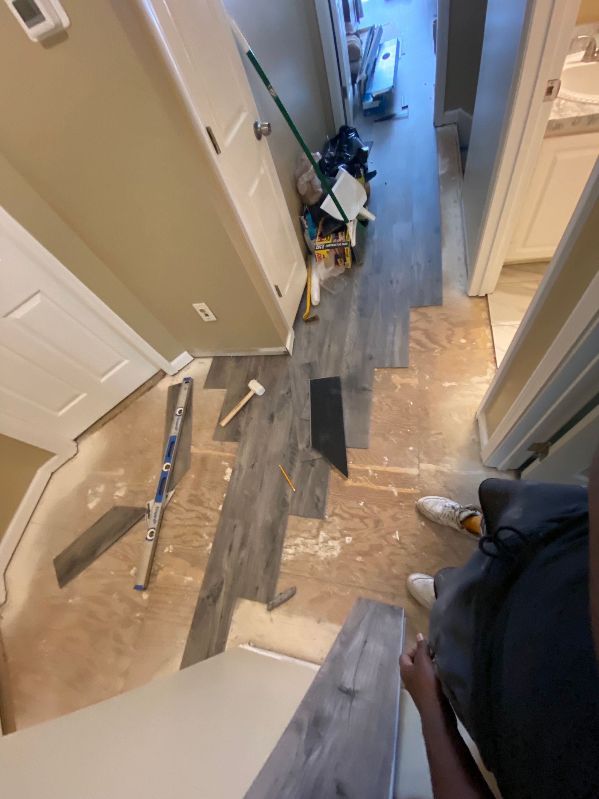 Hallway with flooring being installed; gray plank flooring and tools on the floor.