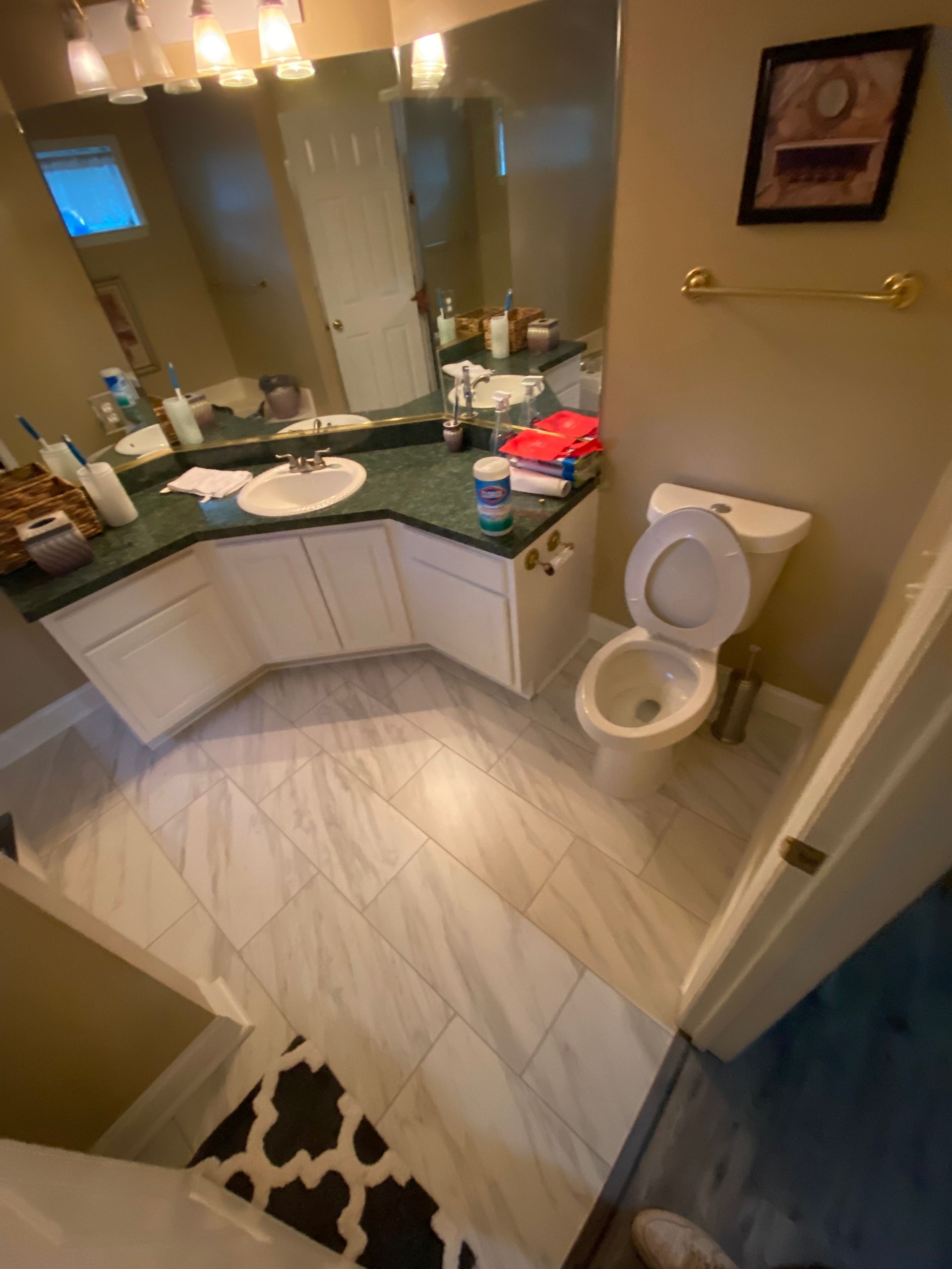 Bathroom with white vanity, toilet, and tile floor; various toiletries and items on the countertop.