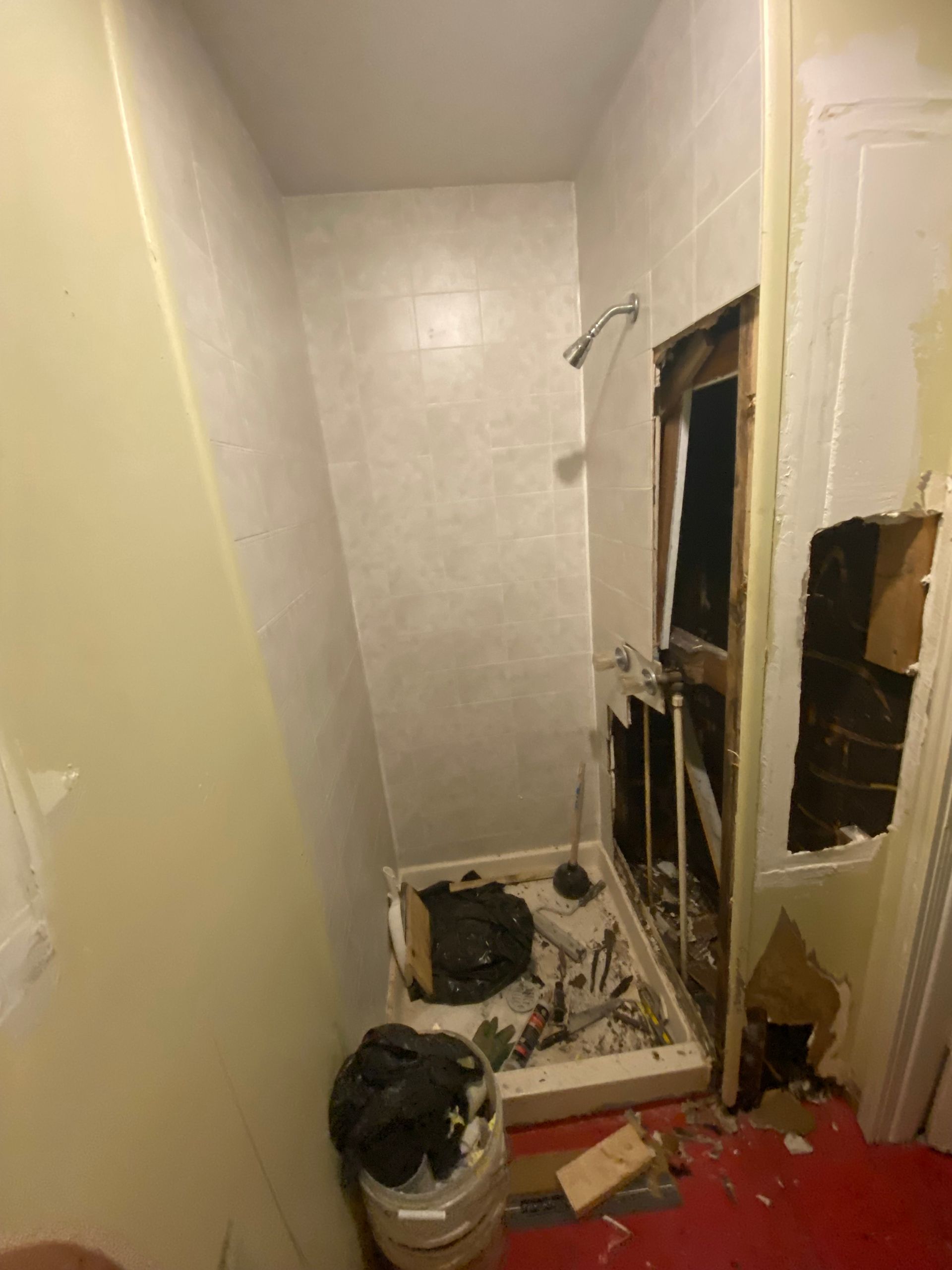 Bathroom with significant damage: missing walls, debris on floor, shower fixtures visible.
