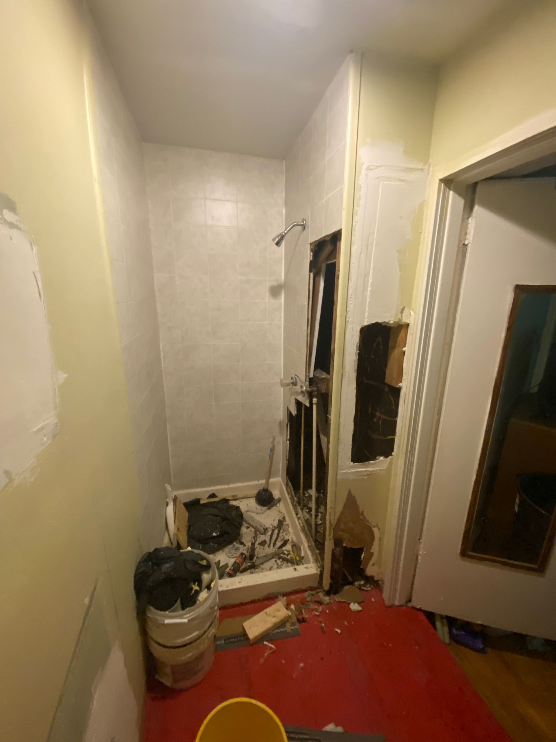 Bathroom under construction; walls damaged, debris on floor, shower base present.