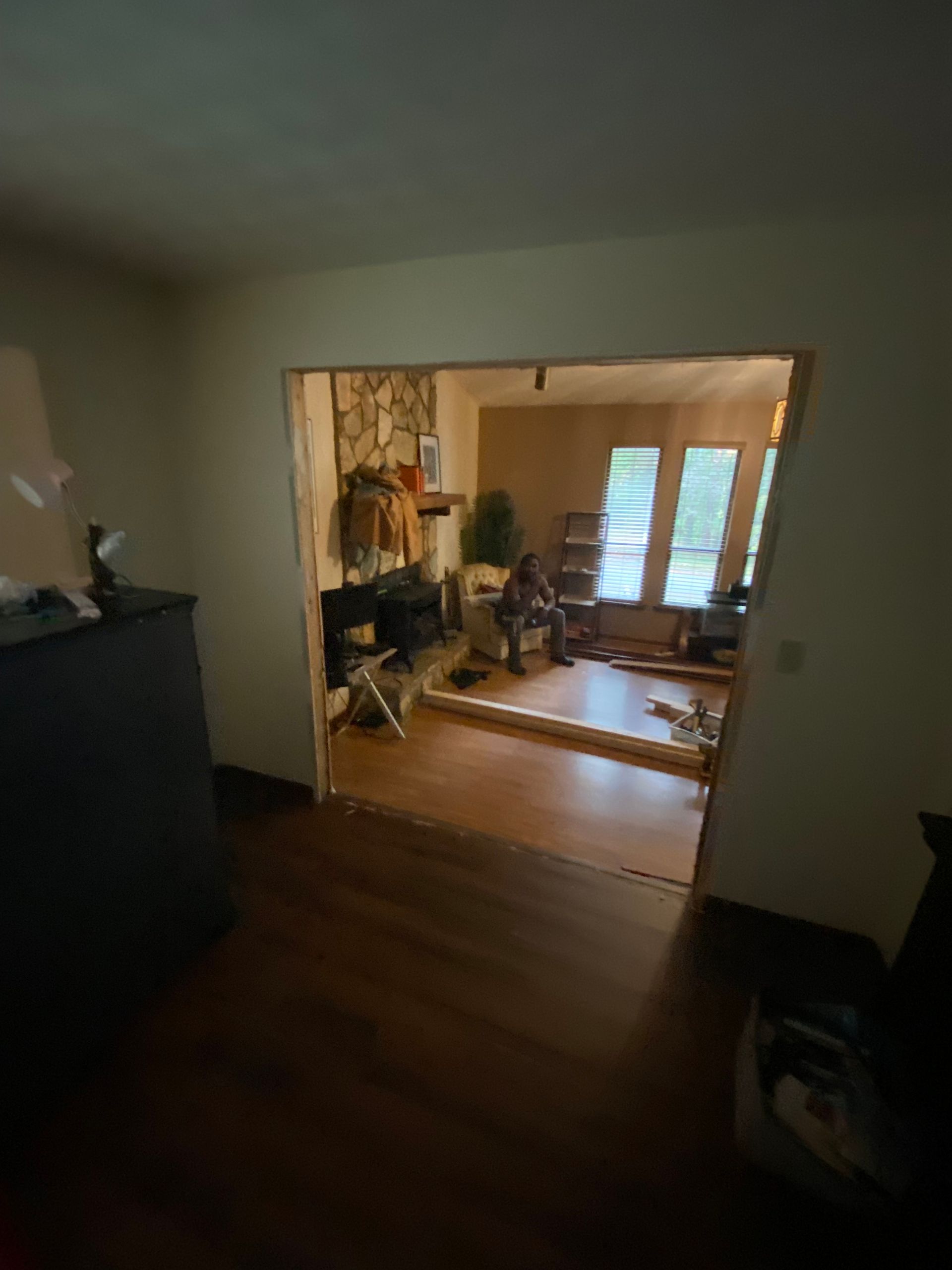 View of an open doorway into a living room, hardwood floors, stone fireplace, and windows.