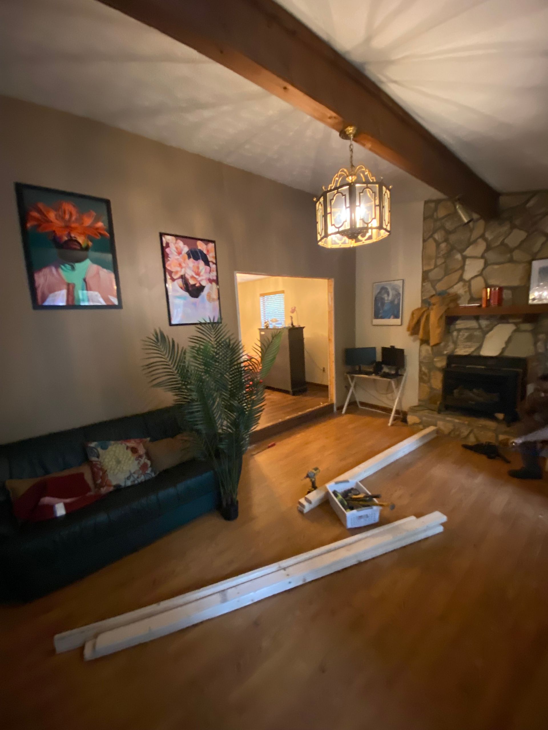 Living room with a dark green couch, stone fireplace, and light fixtures; trim pieces on floor.