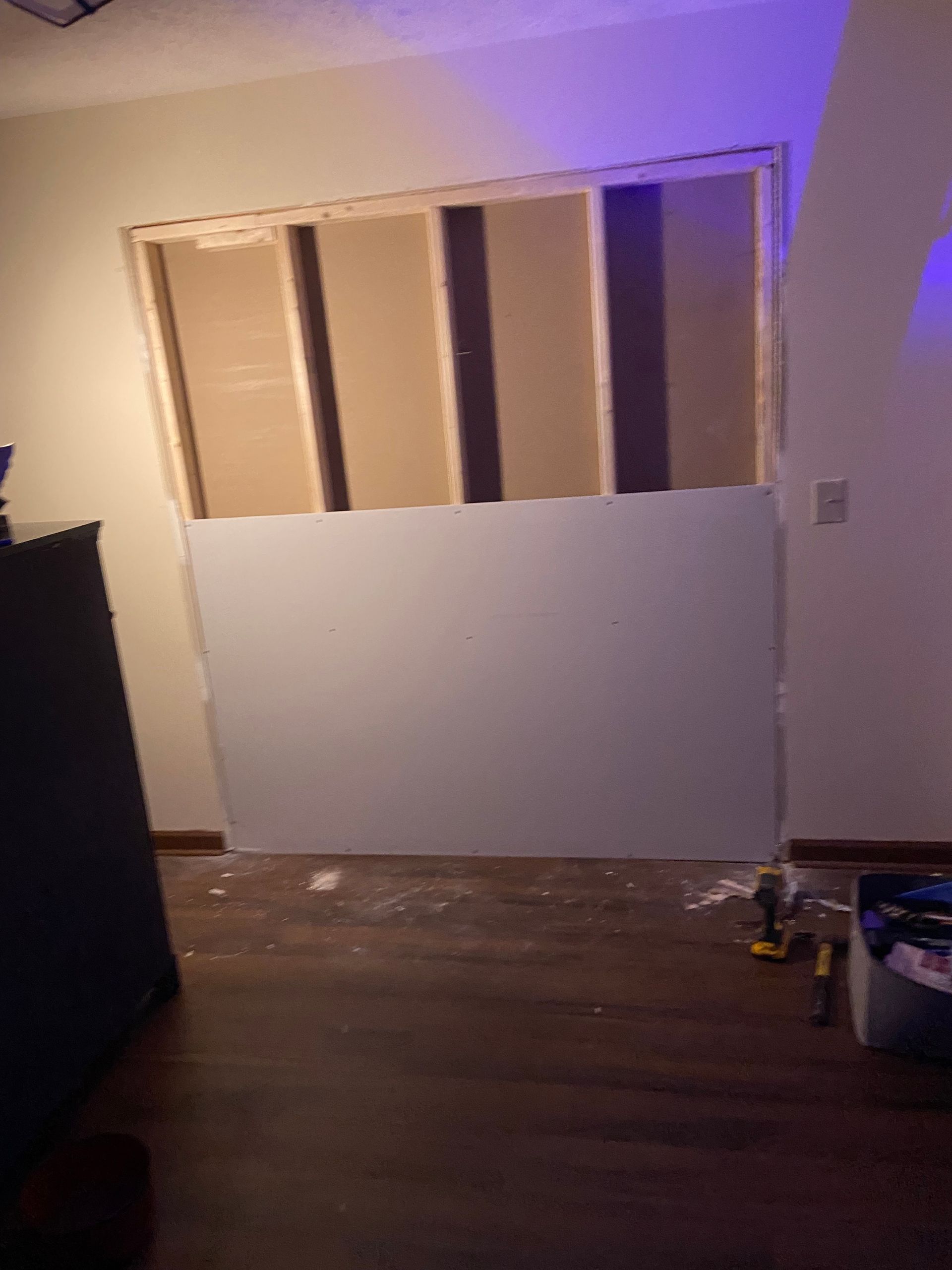 Room with partially installed drywall over an opening, framing exposed; wooden floor, dark dresser.