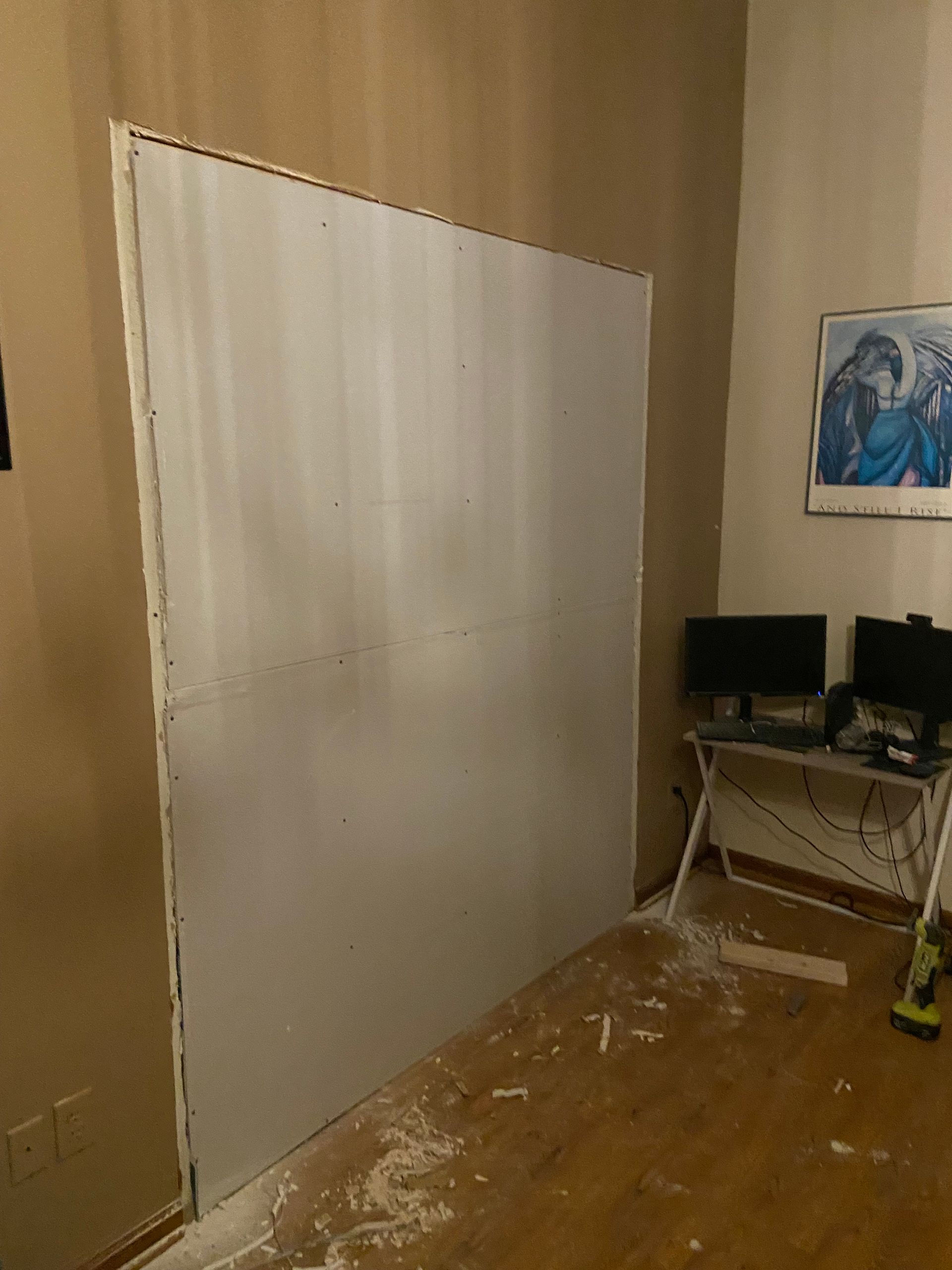 Large white panel in a room, blocking a doorway, drywall dust on floor.
