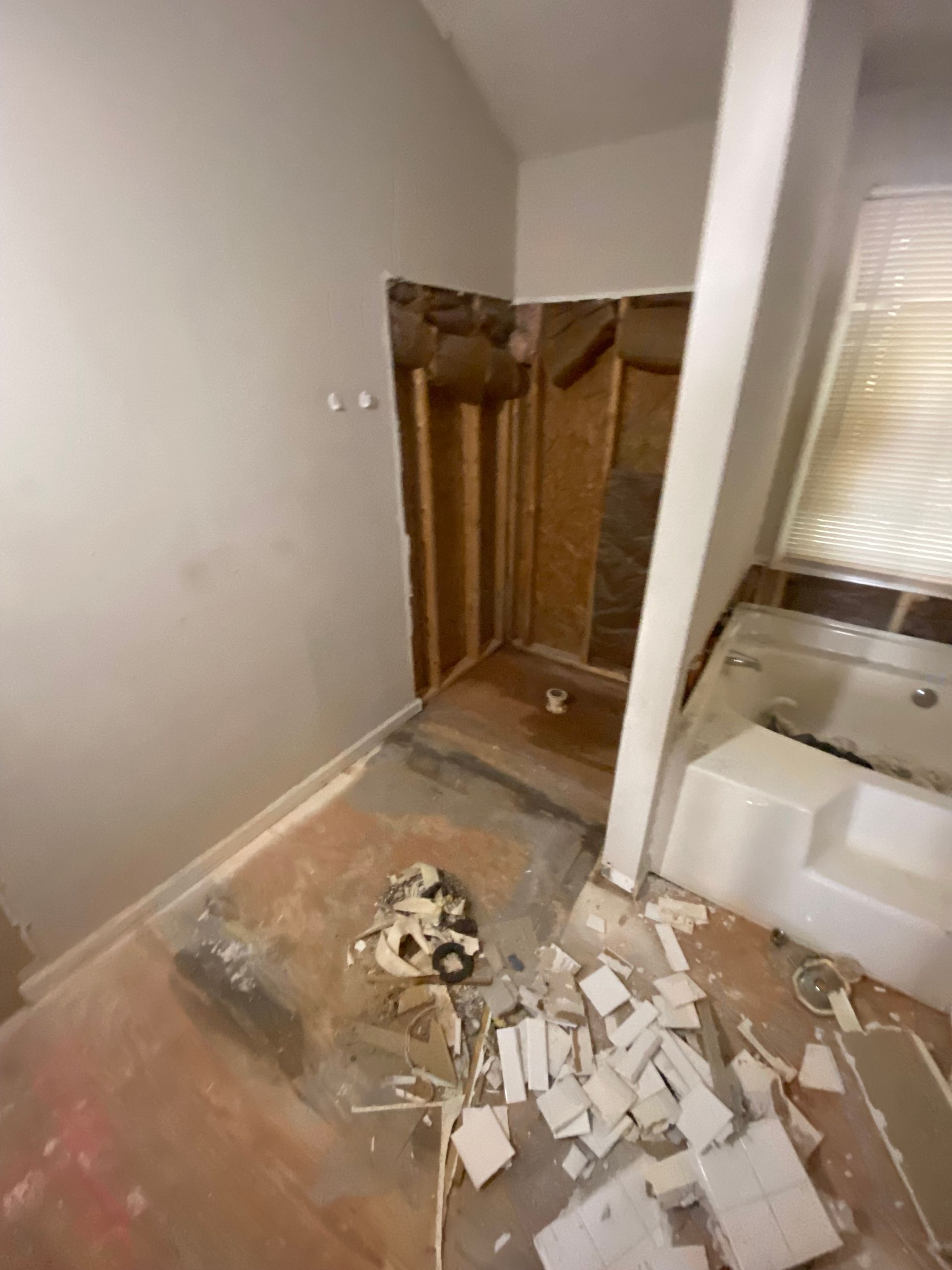 Bathroom renovation in progress; exposed wall studs, debris on floor, and partially built shower area.