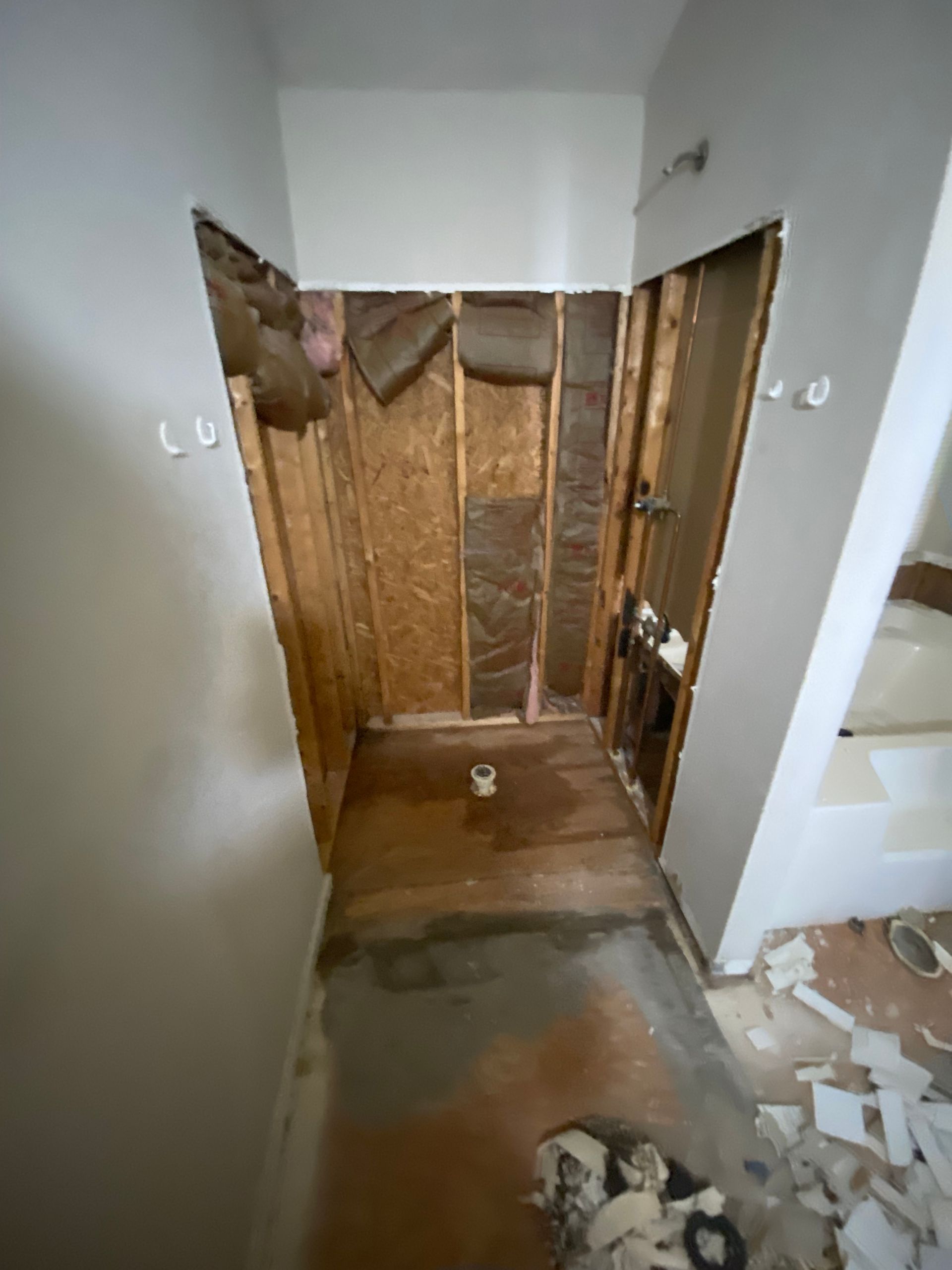 Bathroom shower area under renovation; exposed framing, insulation, and concrete floor.