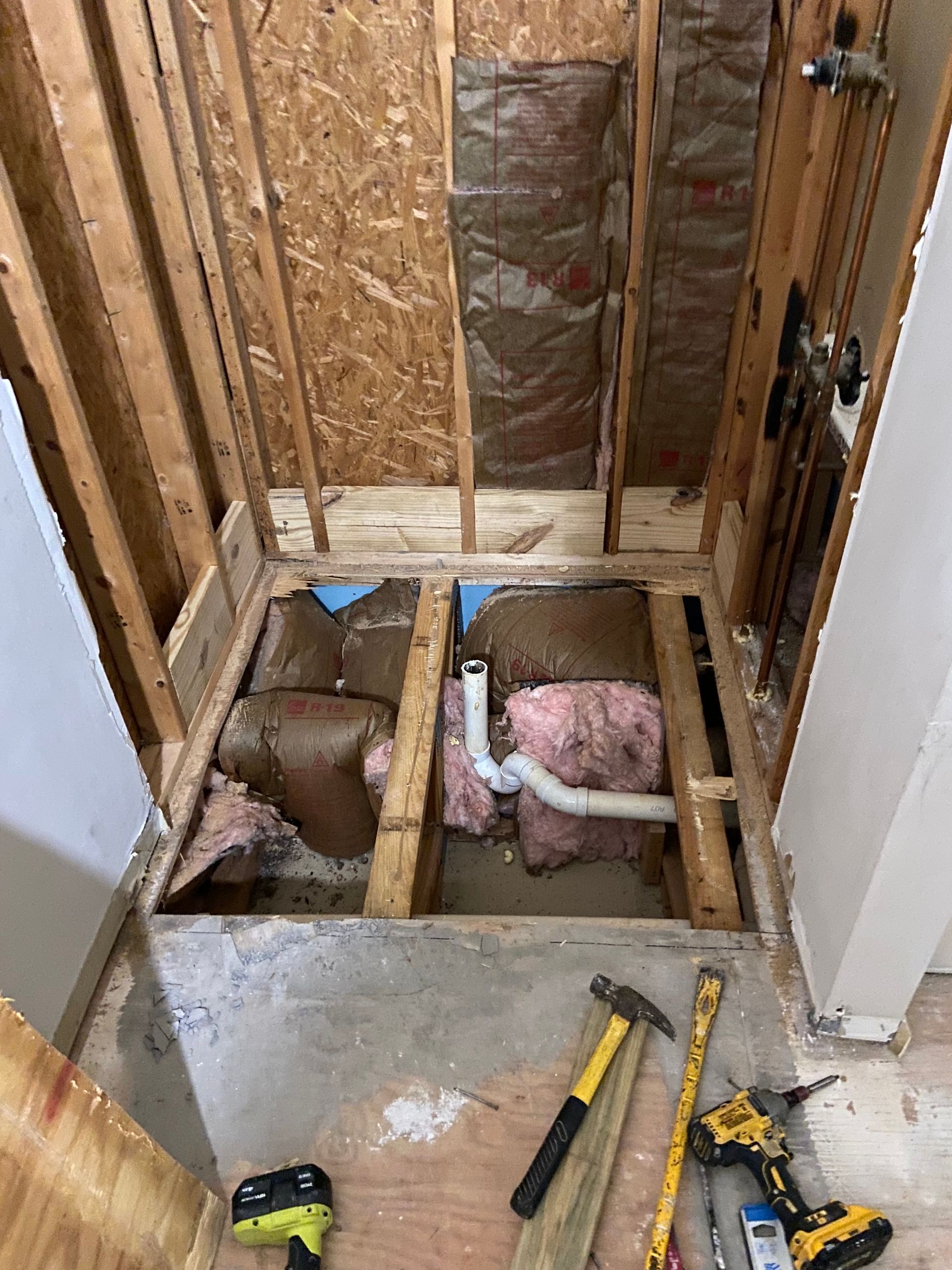 Bathroom renovation in progress, framing, insulation, and plumbing exposed. Tools on floor.