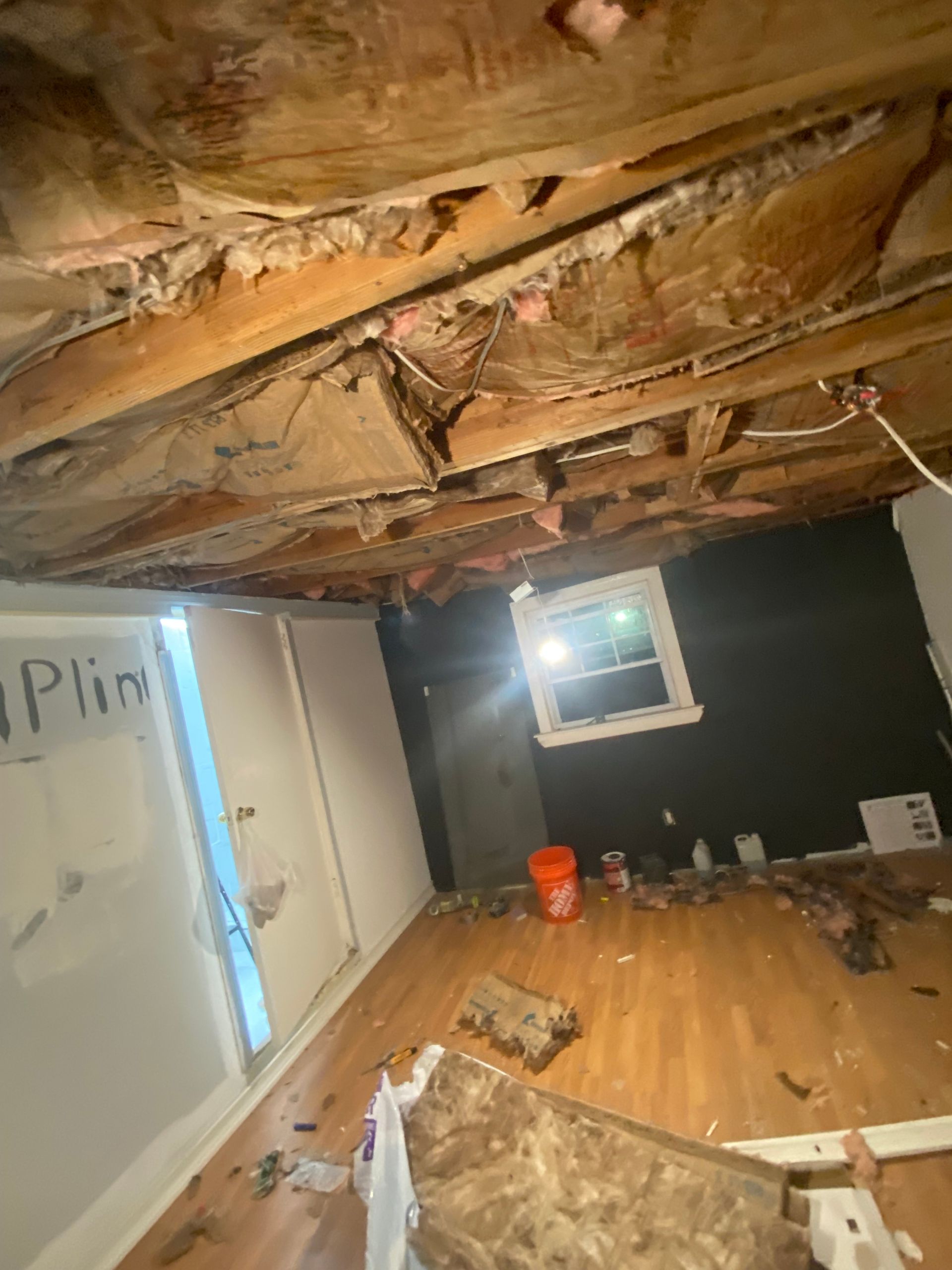 Room with damaged ceiling, debris, and visible insulation; window and door.