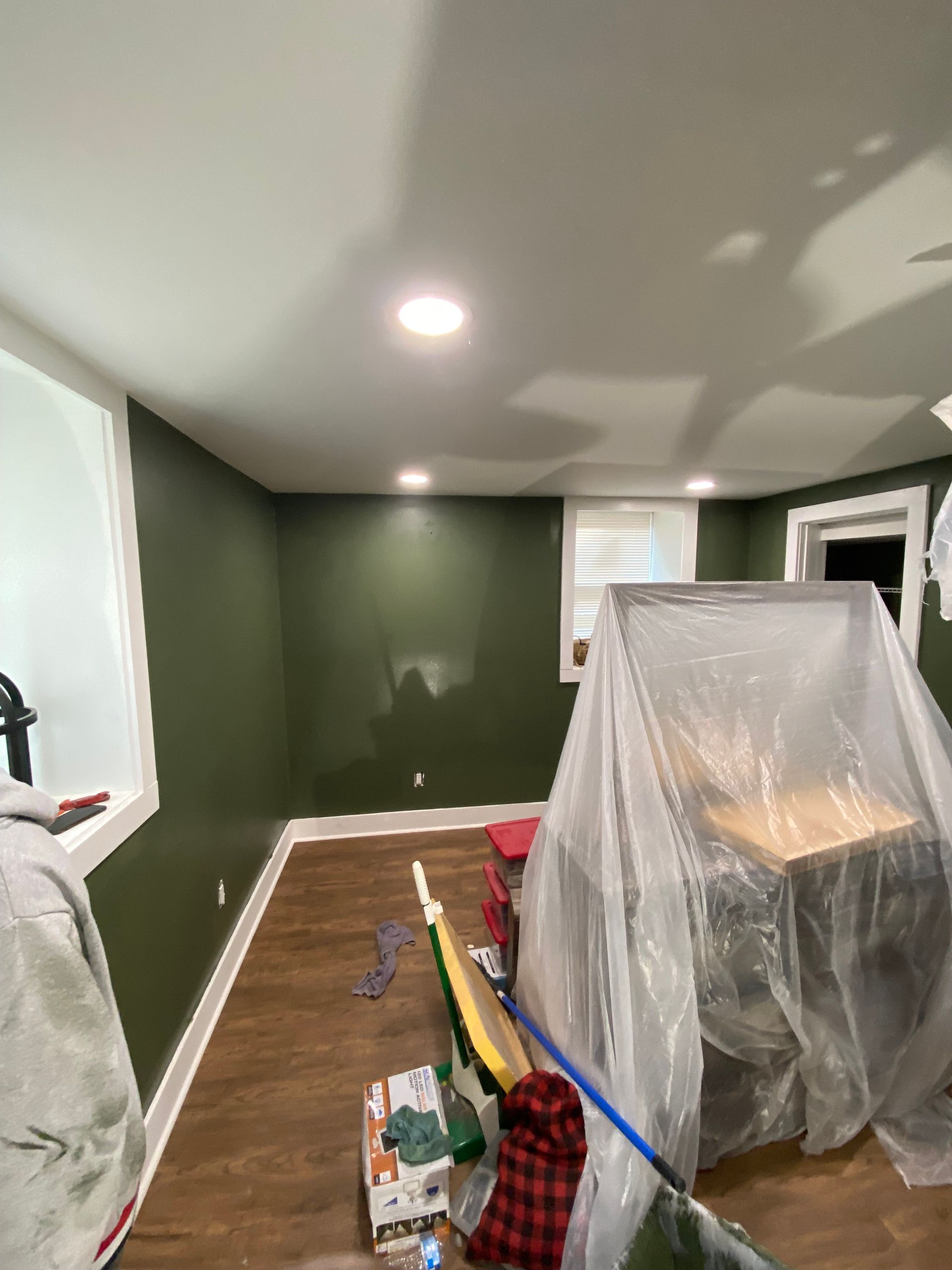 Room with green walls, white trim, and a covered table. Wood flooring. Recessed lighting.