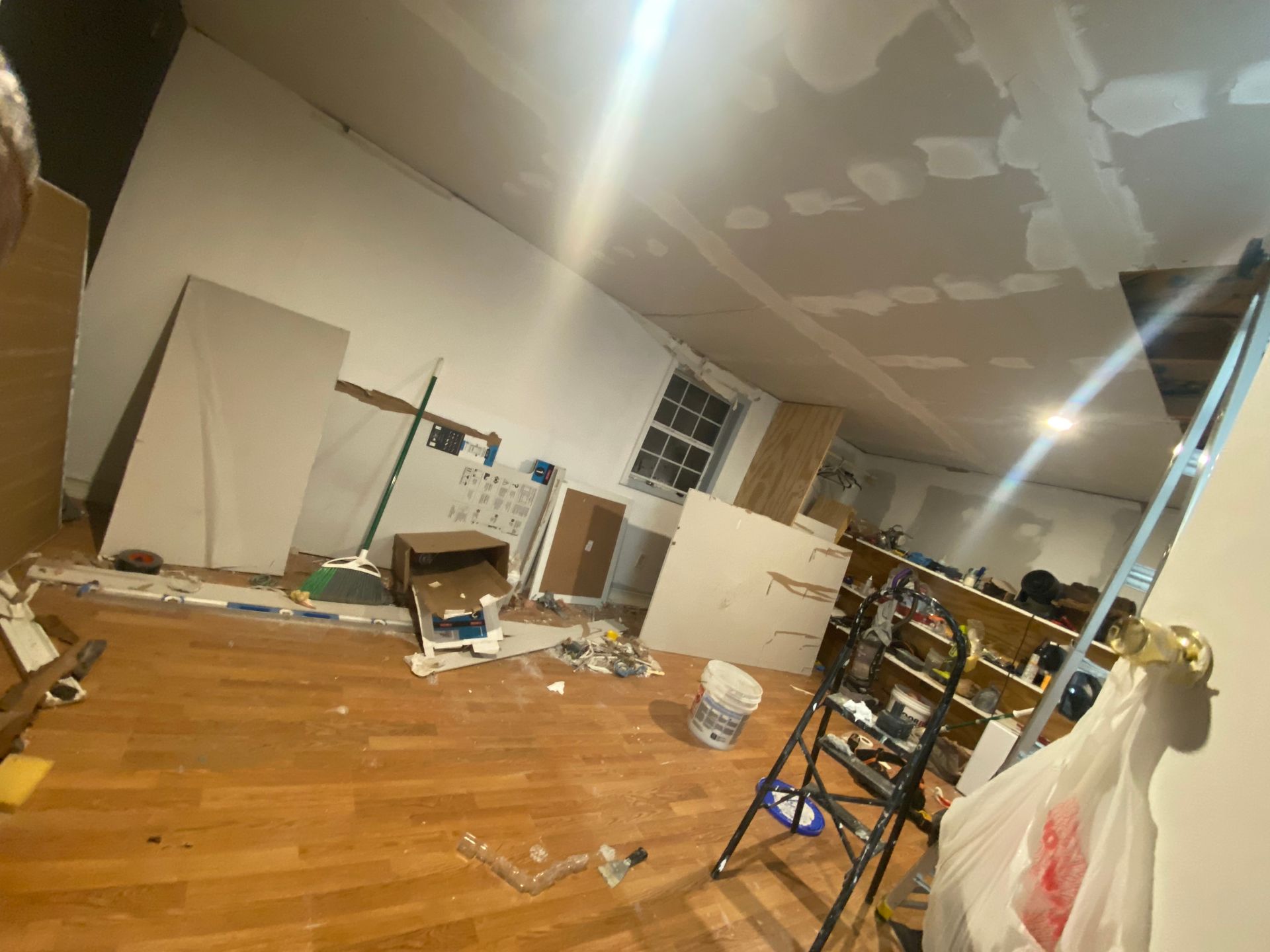 Room under renovation with drywall, ladder, wood floor, and debris.