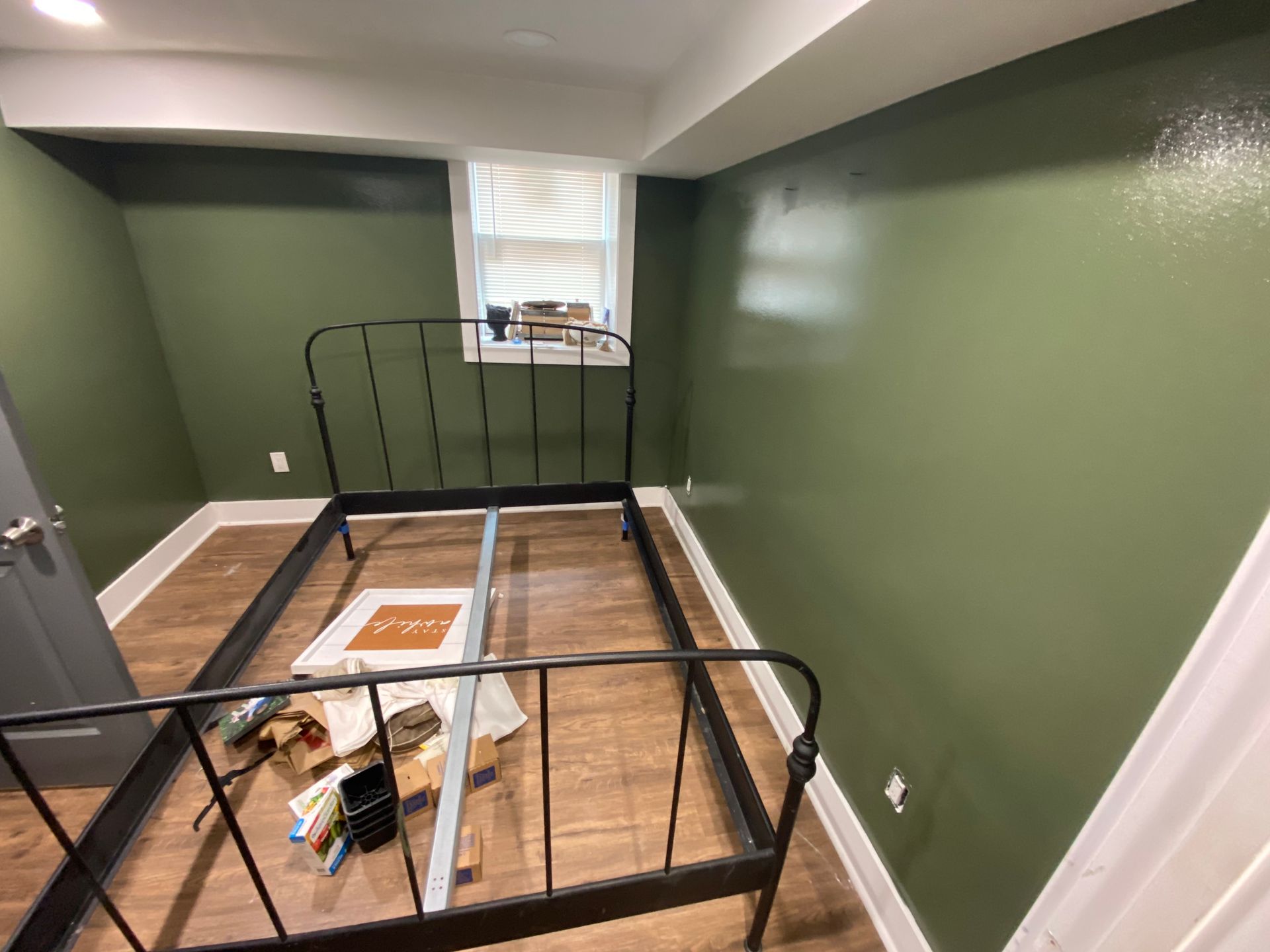 Empty bedroom with green walls, a black metal bed frame, and a small window with blinds.