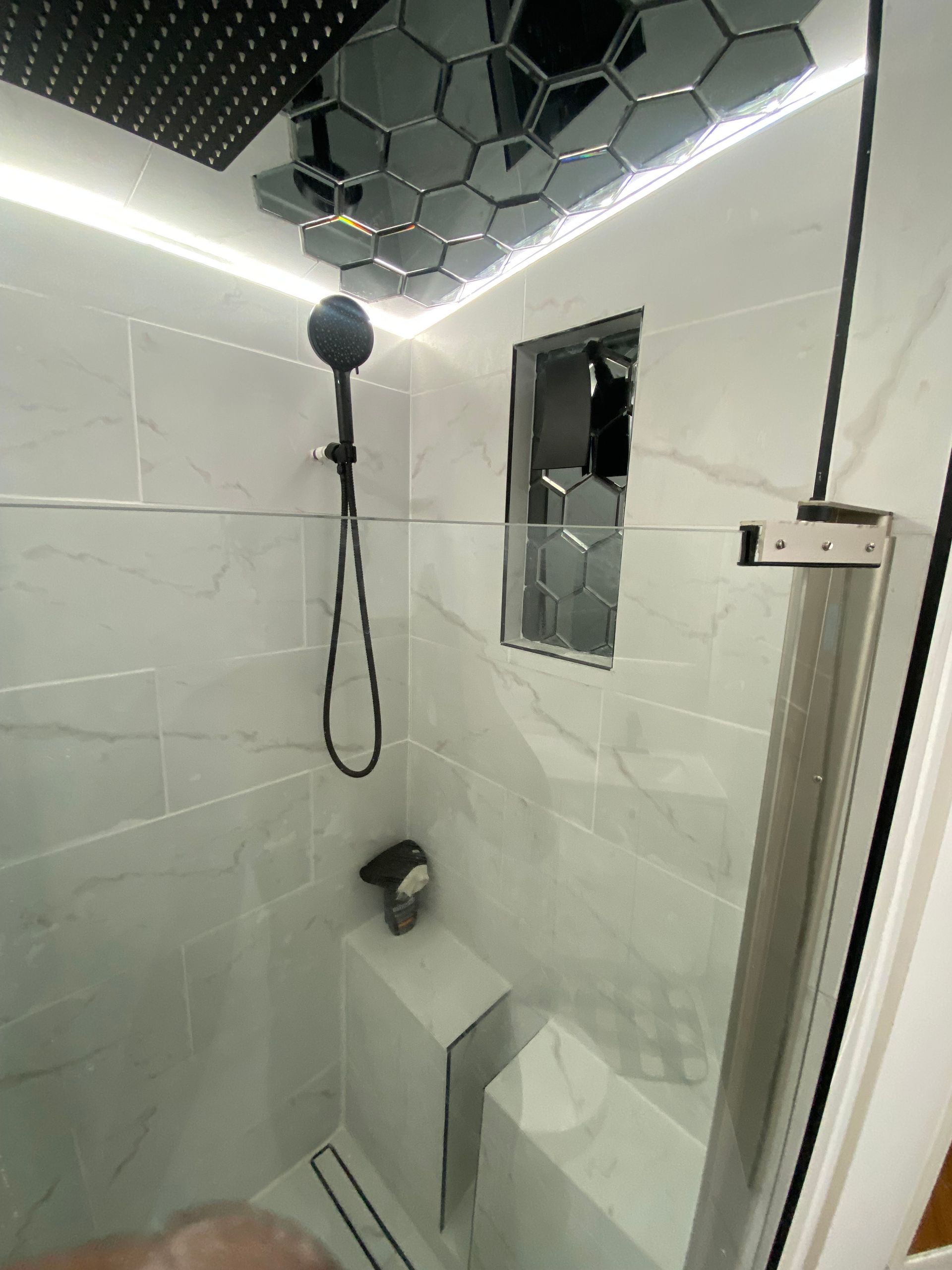 Shower with white tile walls, black fixtures, and a mirrored hexagonal tile ceiling.