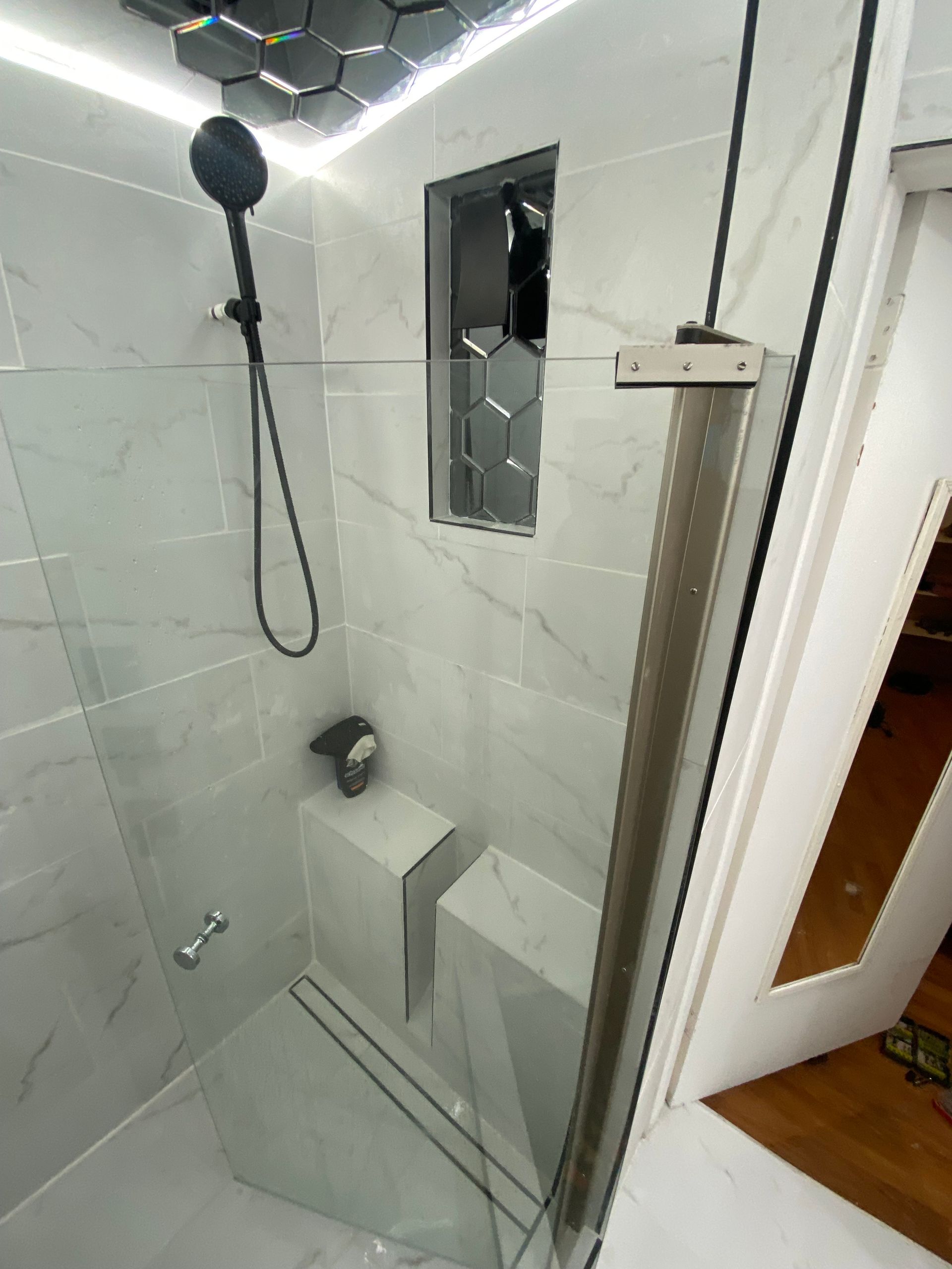 A modern shower with white marble-like tiles, a black showerhead, and a glass door.
