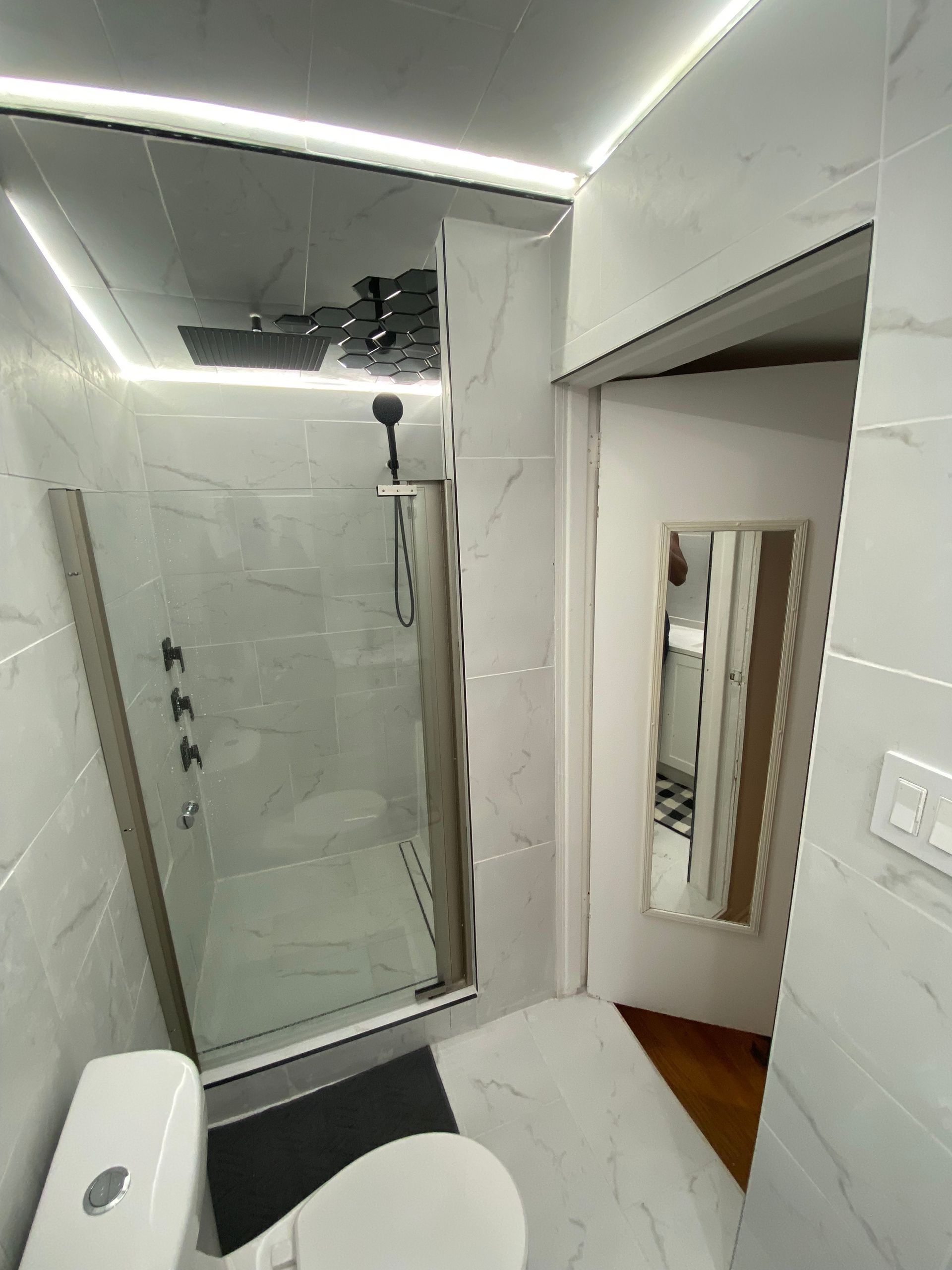Modern bathroom with walk-in shower, white tile, toilet, and doorway with mirror. LED lighting.