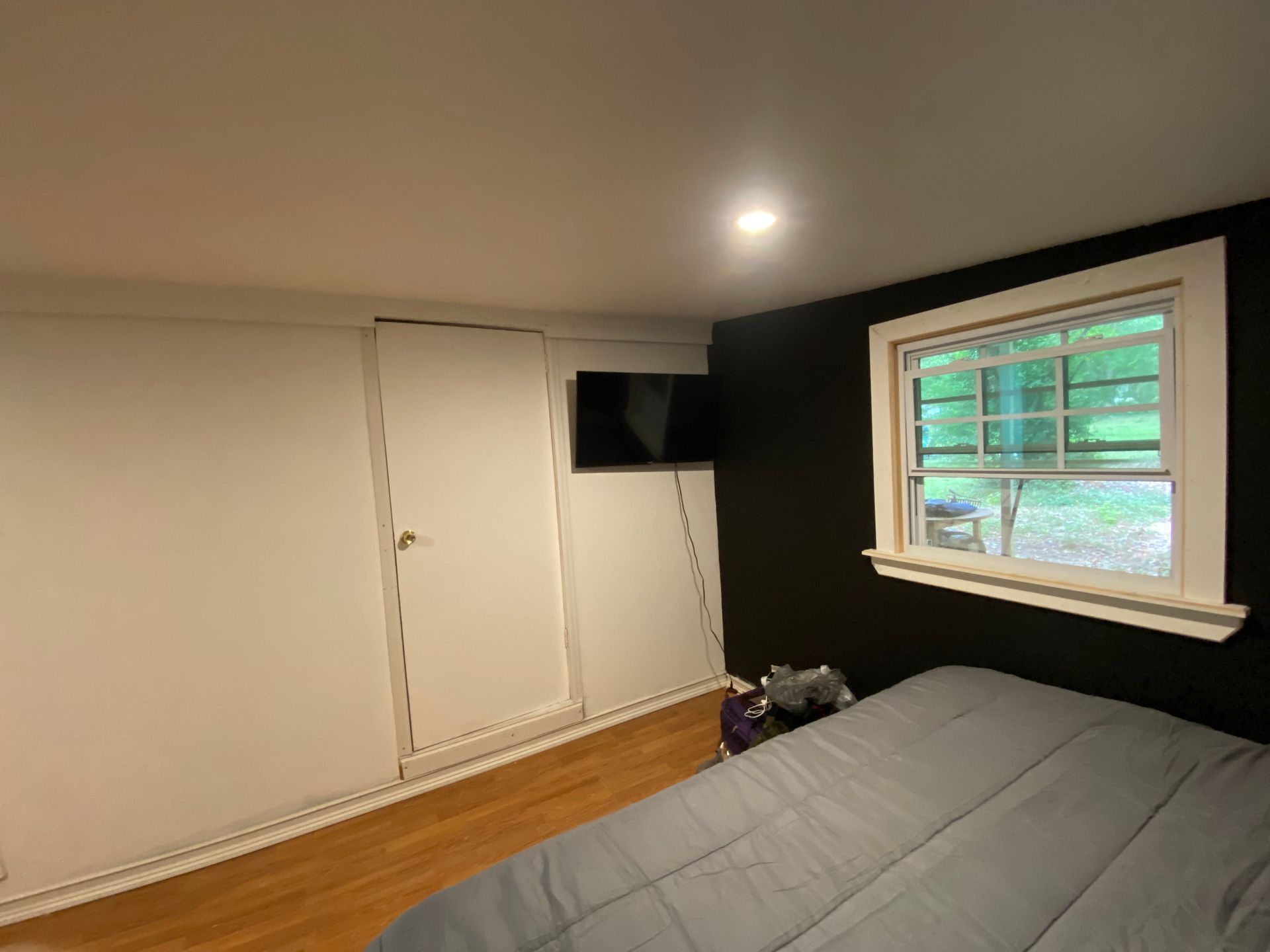 Bedroom with white closet, black wall, window, TV, and bed.