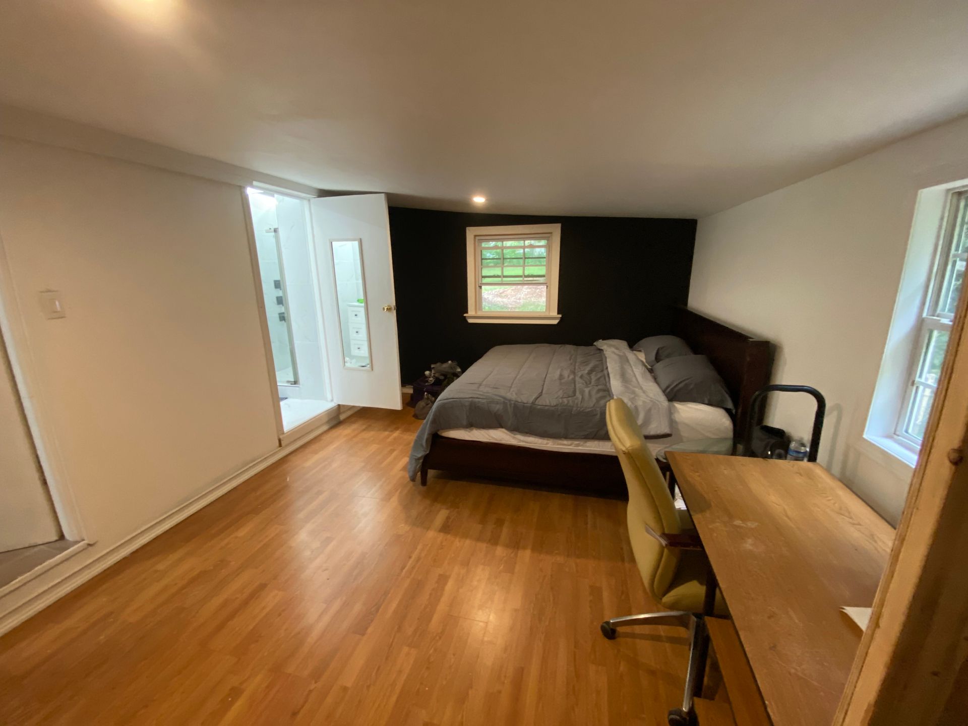 Bedroom with wood floors, bed with gray bedding, desk, black accent wall, window, and white door.