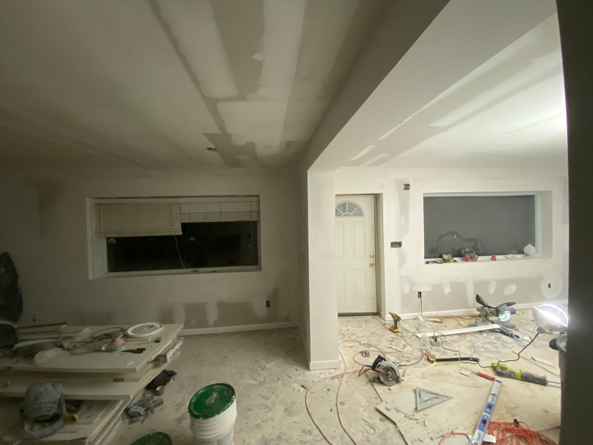 Interior renovation: Drywall installed on walls and ceiling; tools and debris on floor.