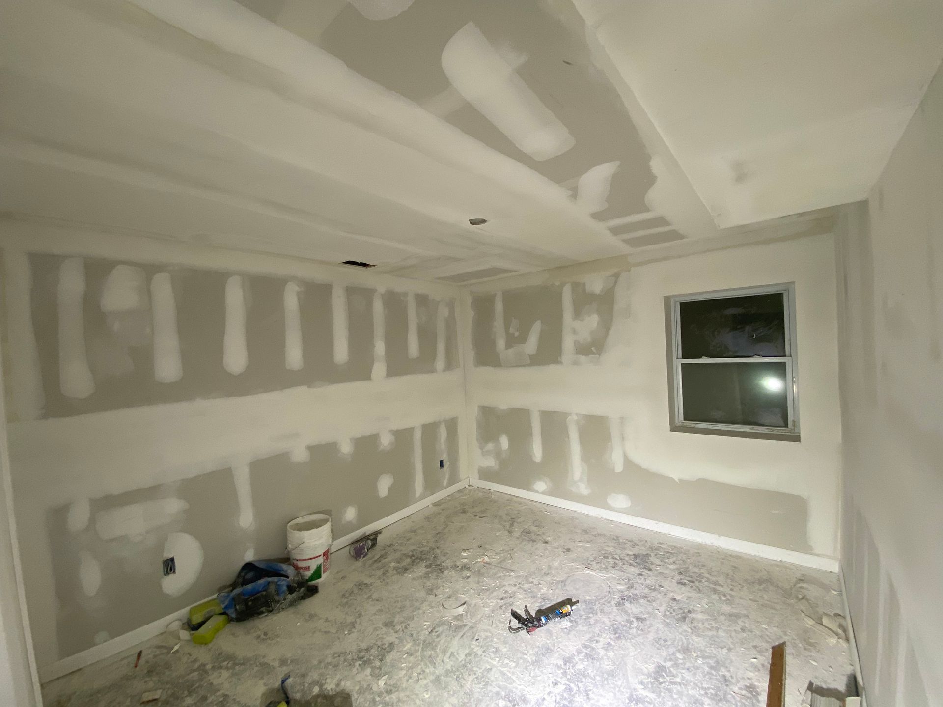 Room under construction, drywall installed on walls and ceiling, visible window.
