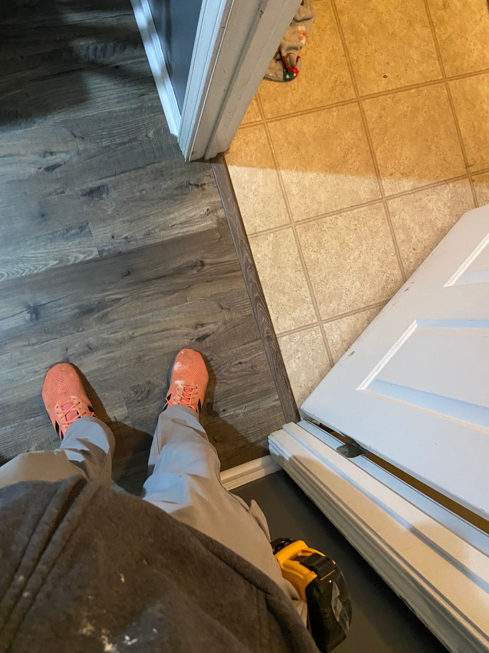 Person standing in doorway with dark wood and tile flooring. Light pink shoes.