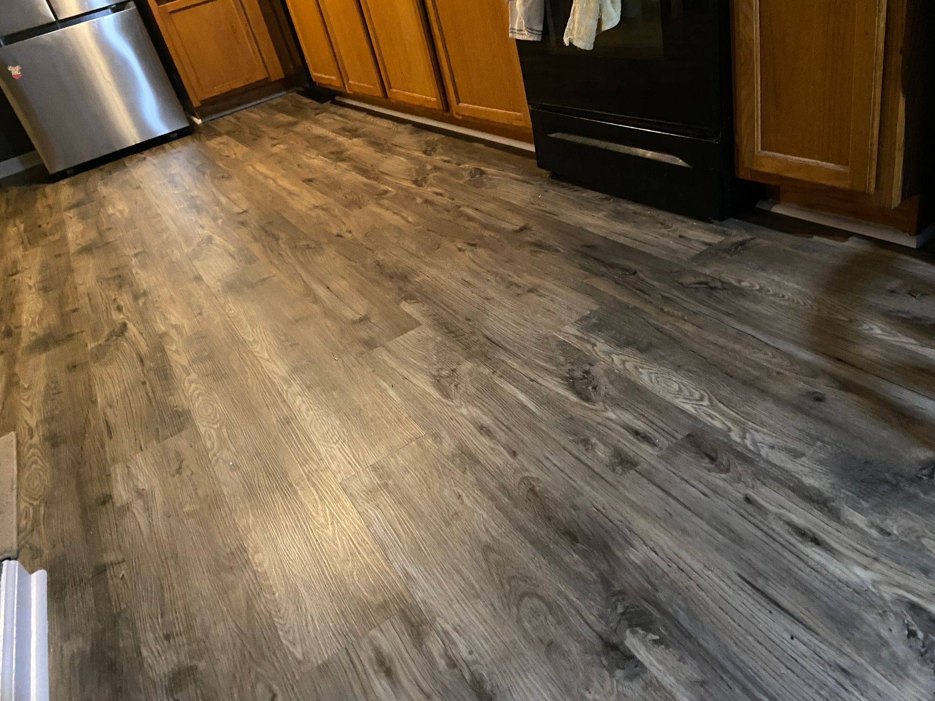 Dark gray wood-look flooring in a kitchen, with cabinets and appliances visible.