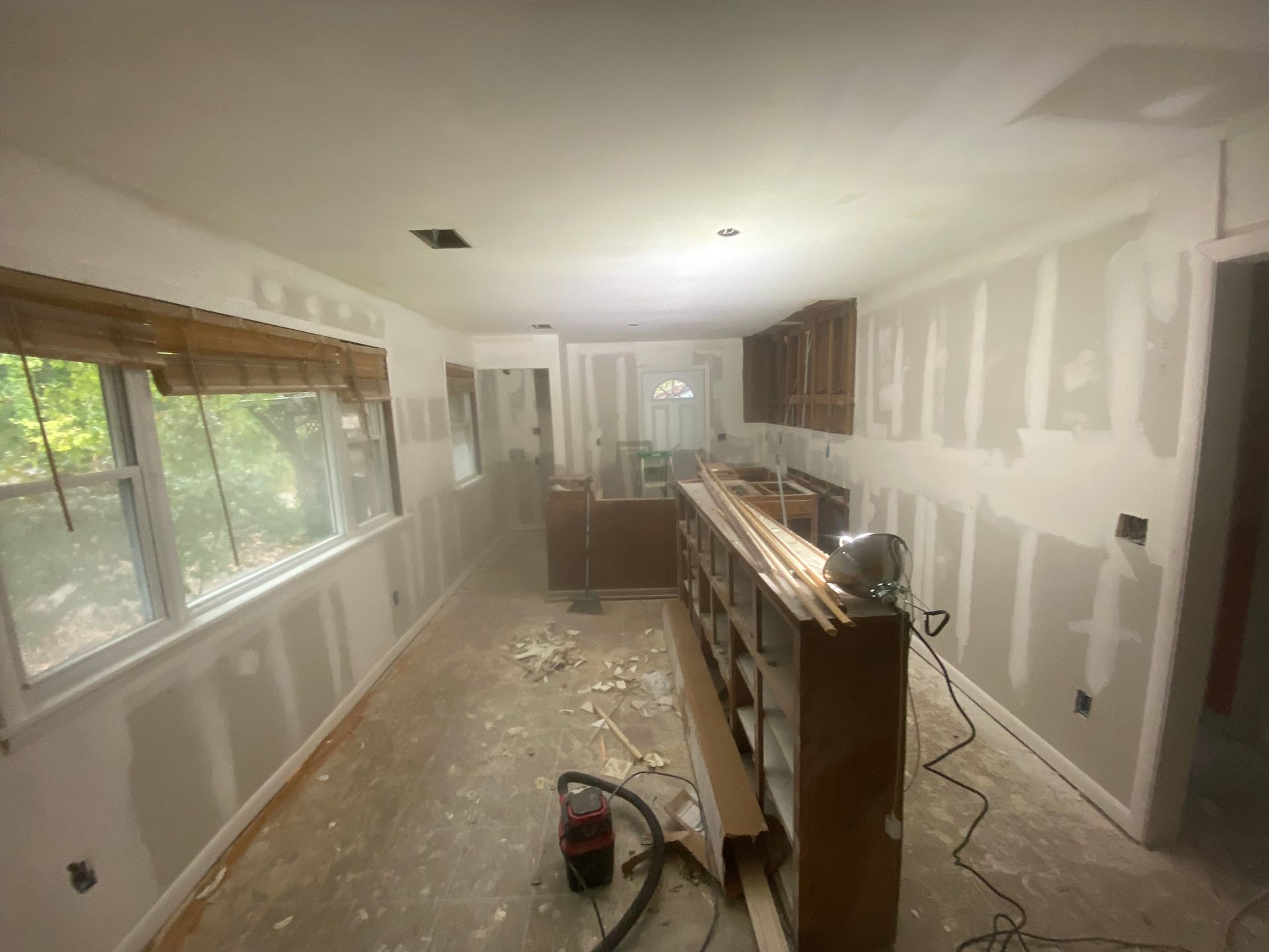 Kitchen under renovation: drywall installed, cabinets in place, debris on floor.