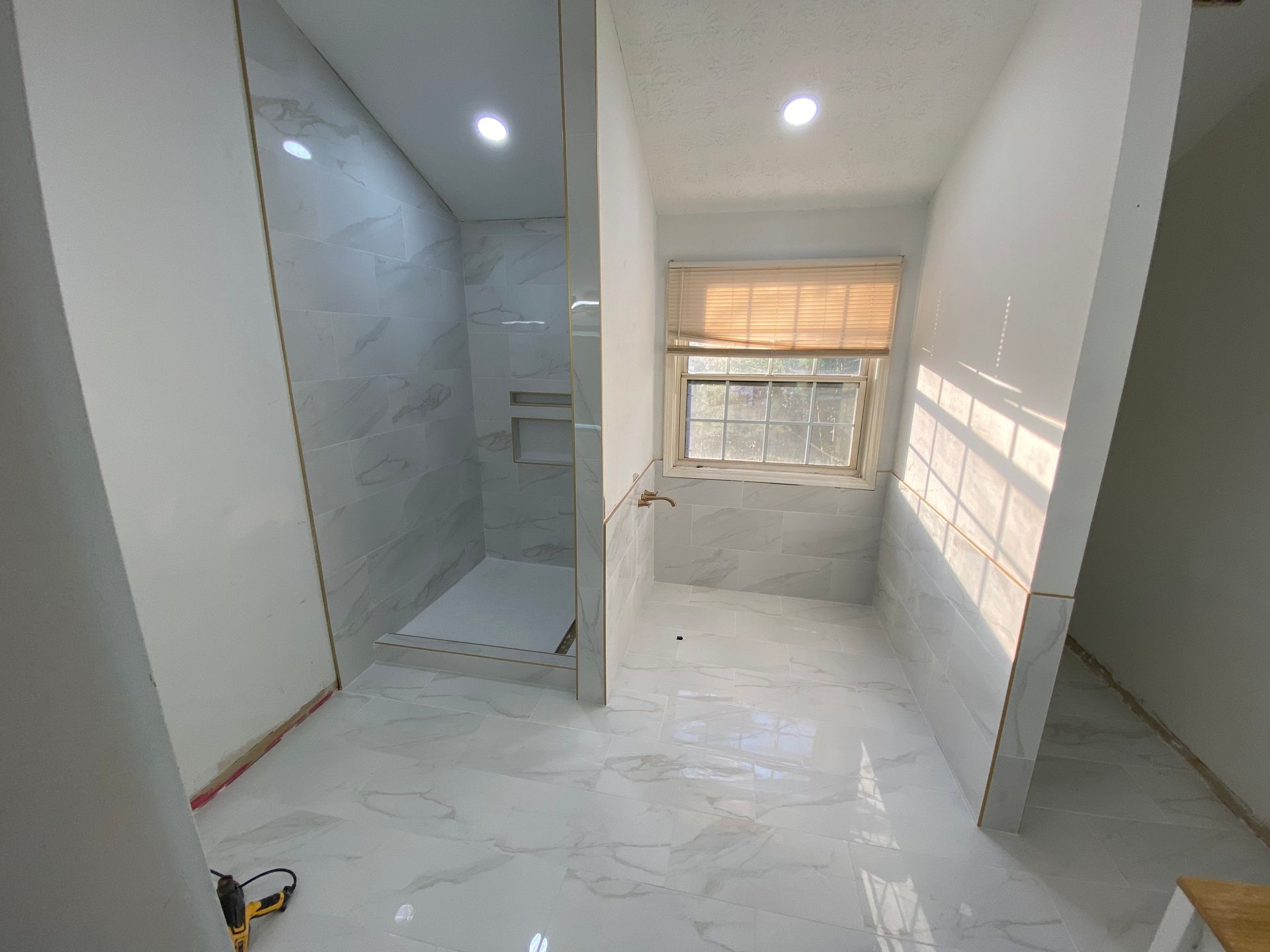 Bathroom under construction with shower, window, and tile flooring.