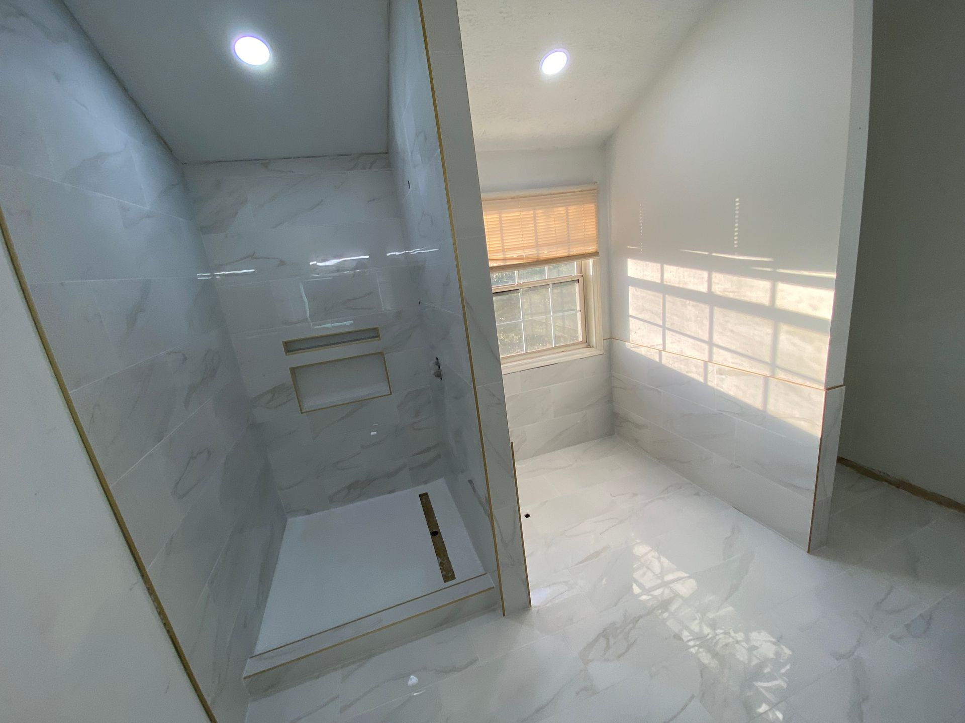 A modern, newly renovated bathroom with a shower stall, window, and marble-like tile.