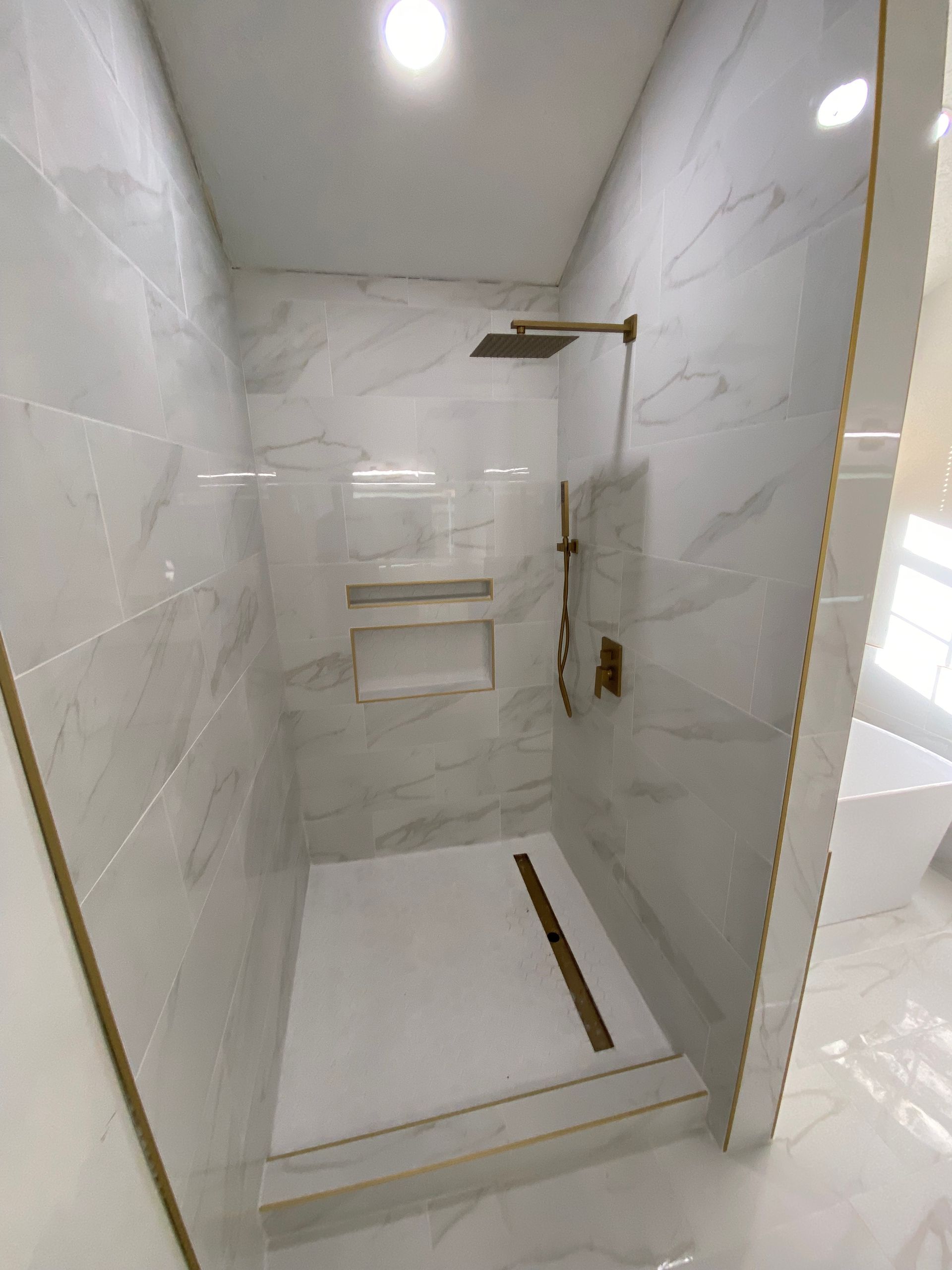 Modern shower with marble-look tiles, gold fixtures, and built-in shelves.