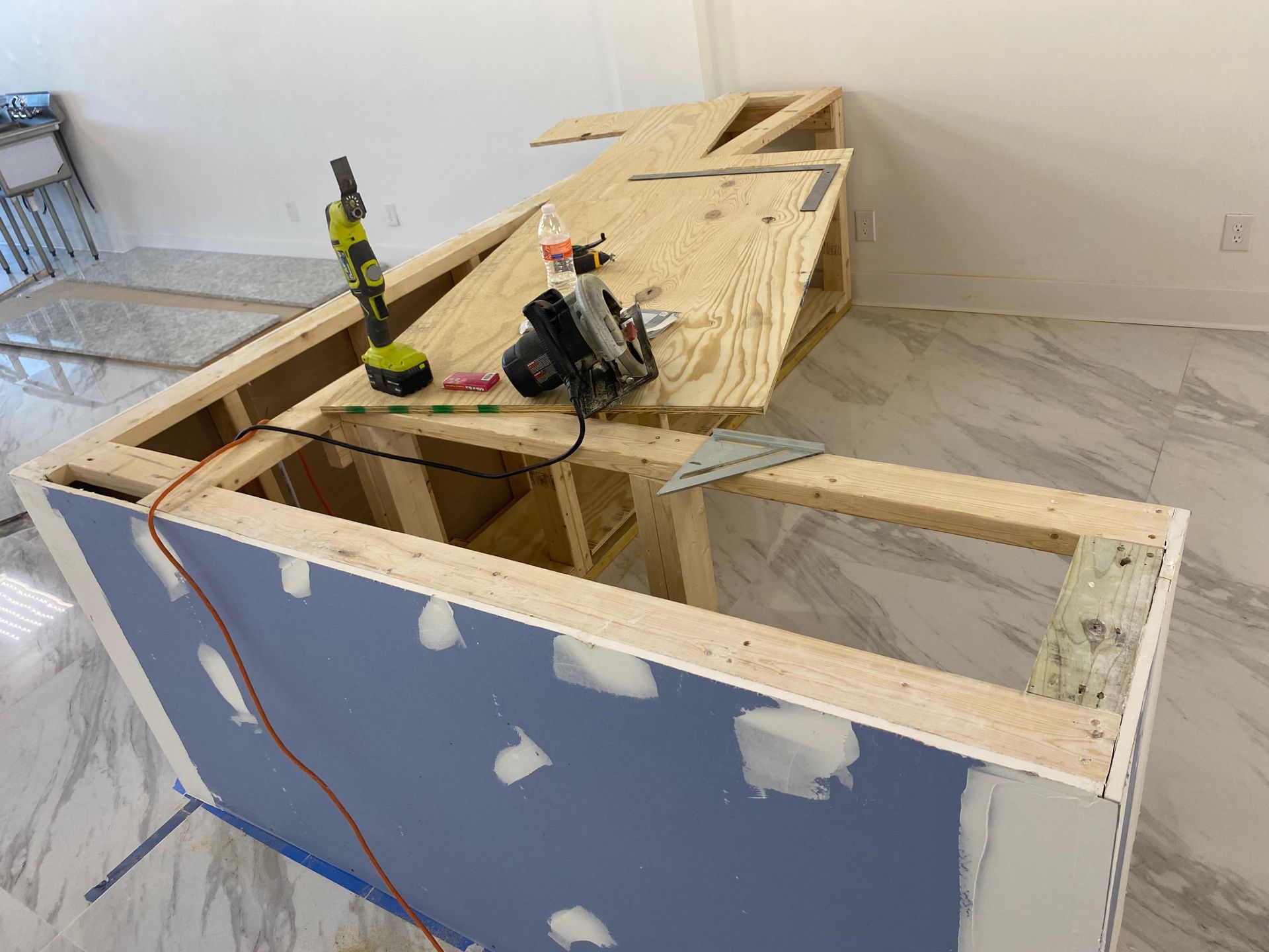 Construction of a bar with wooden frame and blue drywall. Tools and plywood on top.