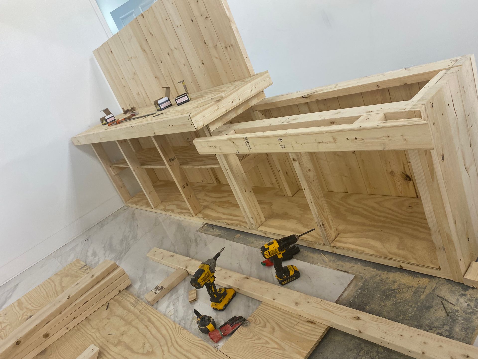 Wooden cabinet being assembled with power tools in a room.
