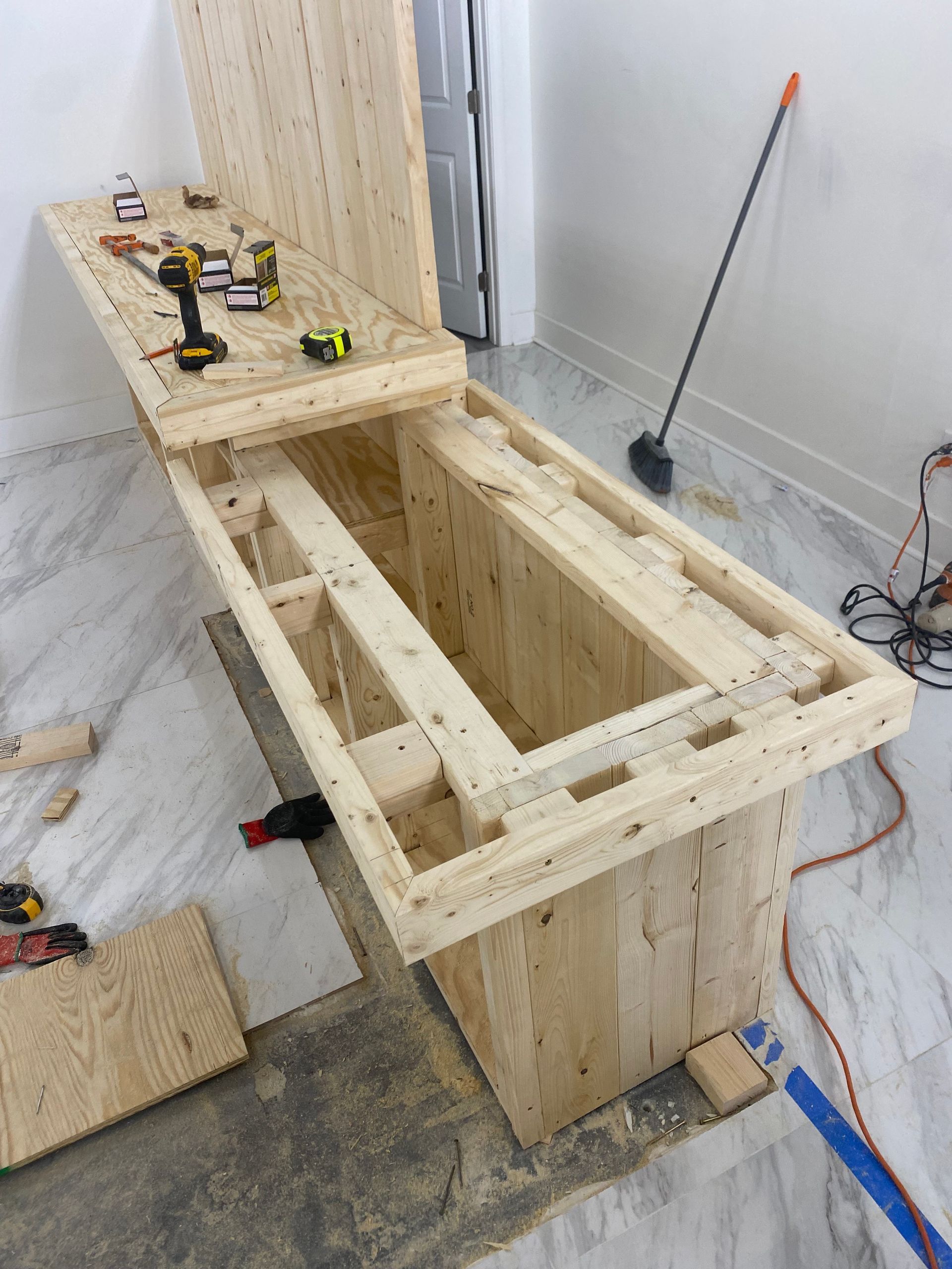 A partially built wooden box-shaped structure with a hinged top, in a room with a concrete floor. Tools are visible.