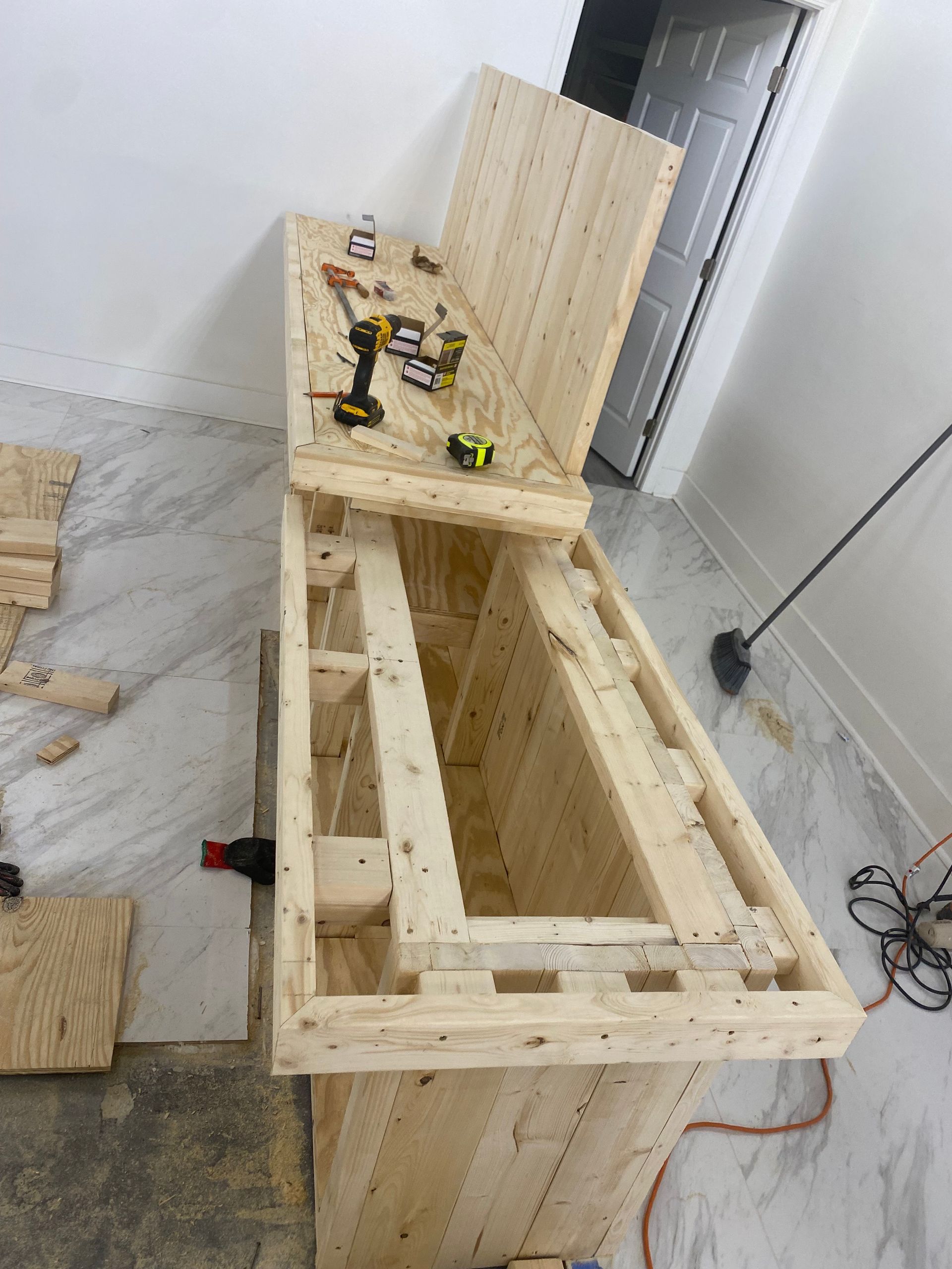 Wooden structure being built indoors with tools on top, partially open.