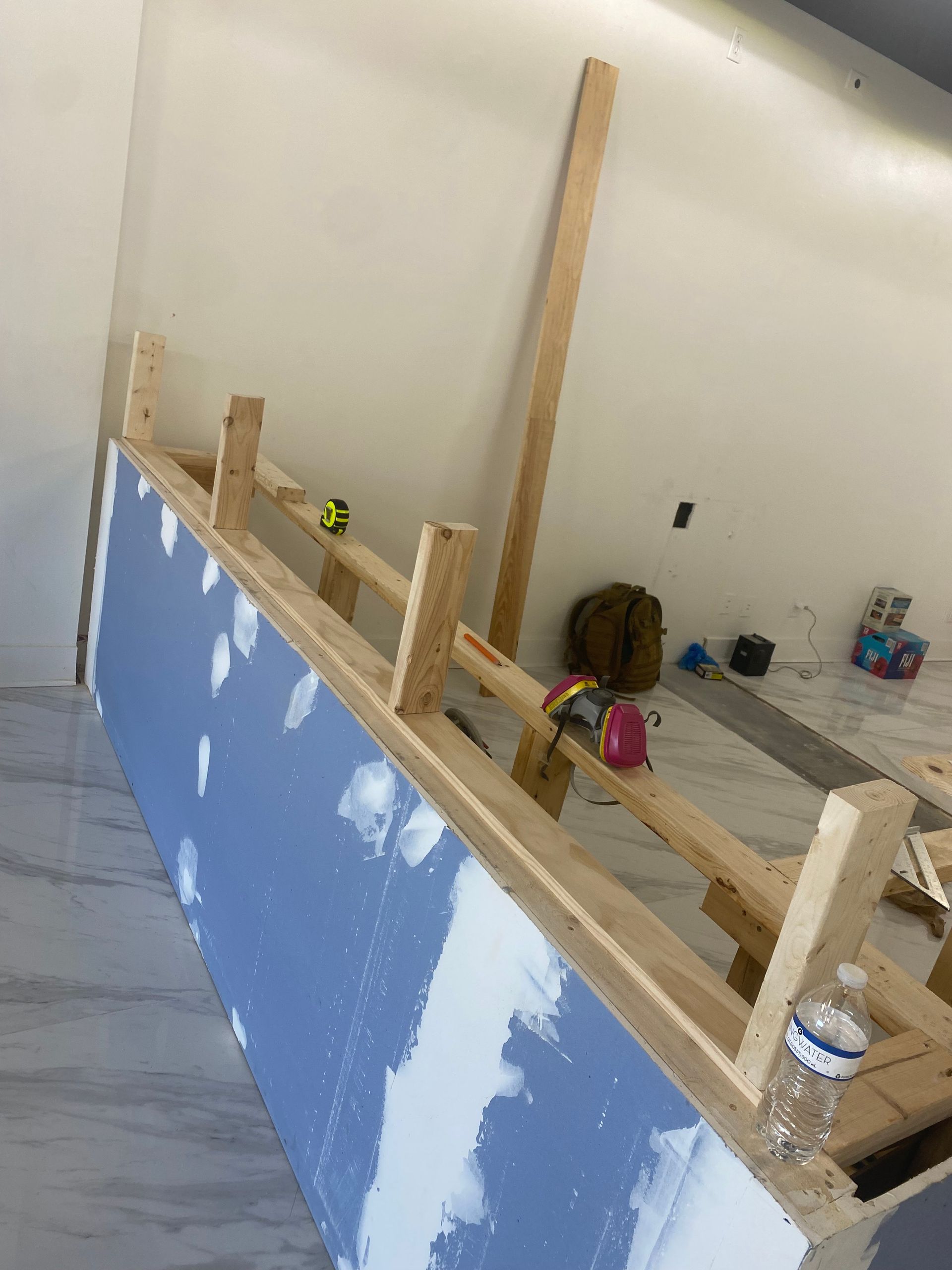 Construction of a built-in bench. Wood framing and drywall are visible. Tools and materials are nearby.