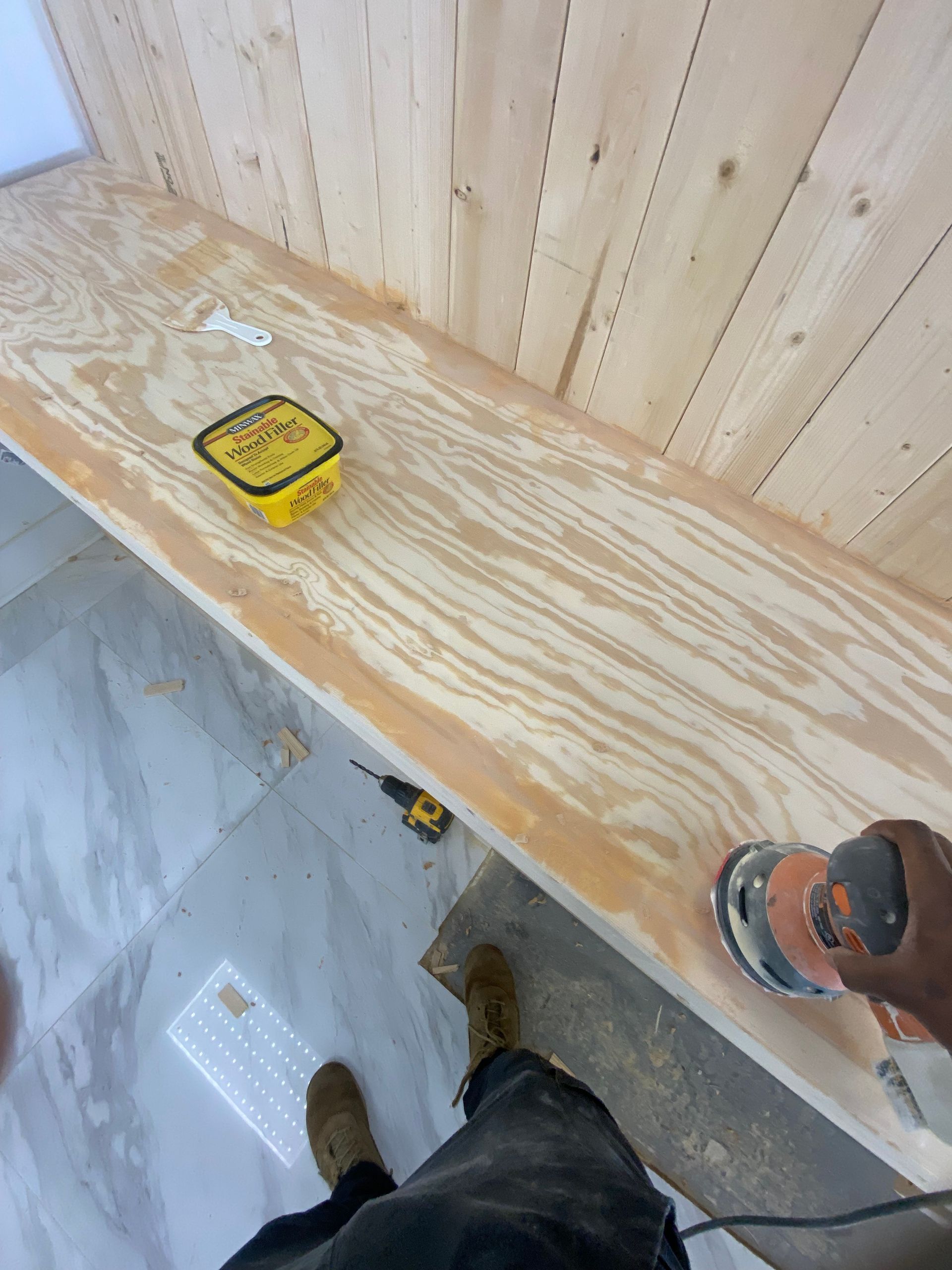 Person sanding a wooden counter with a power sander. Yellow container sits on the counter.