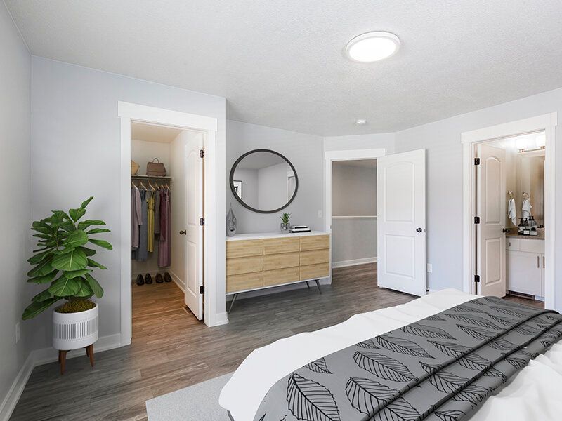 Bedroom in a modern apartment with a dresser, round mirror, and open closet.