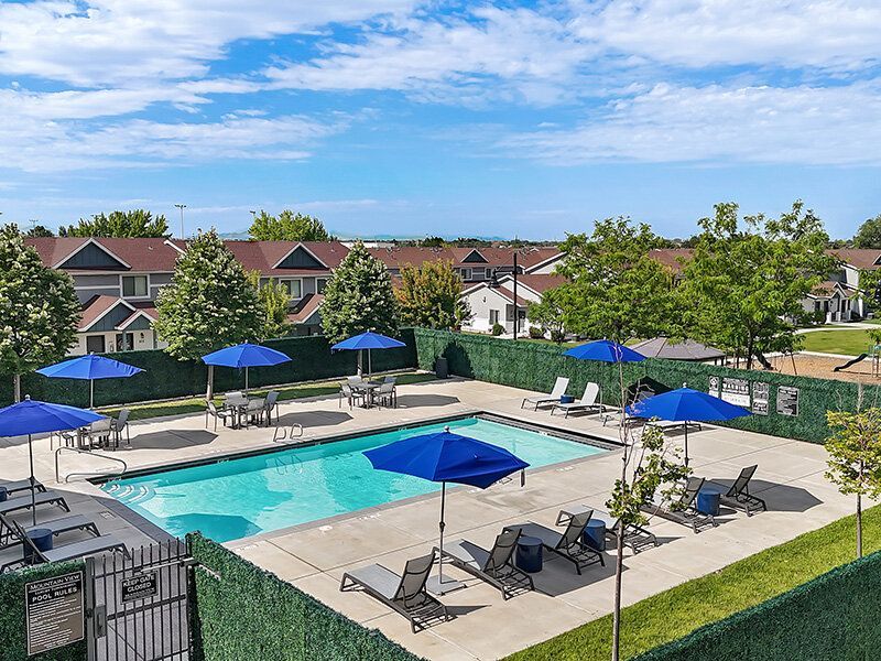 Outdoor community pool area with blue umbrellas and lounge chairs.