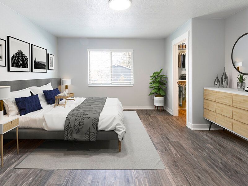 Modern apartment bedroom with a king-size bed, two nightstands, dresser, plant, and open closet.
