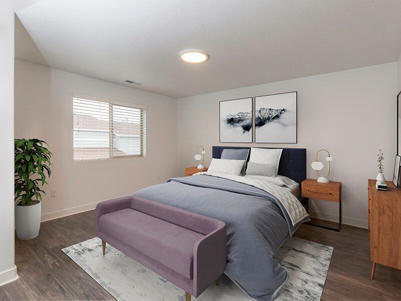 Bright apartment bedroom with a queen bed, two nightstands, a purple bench at the foot, and a plant.