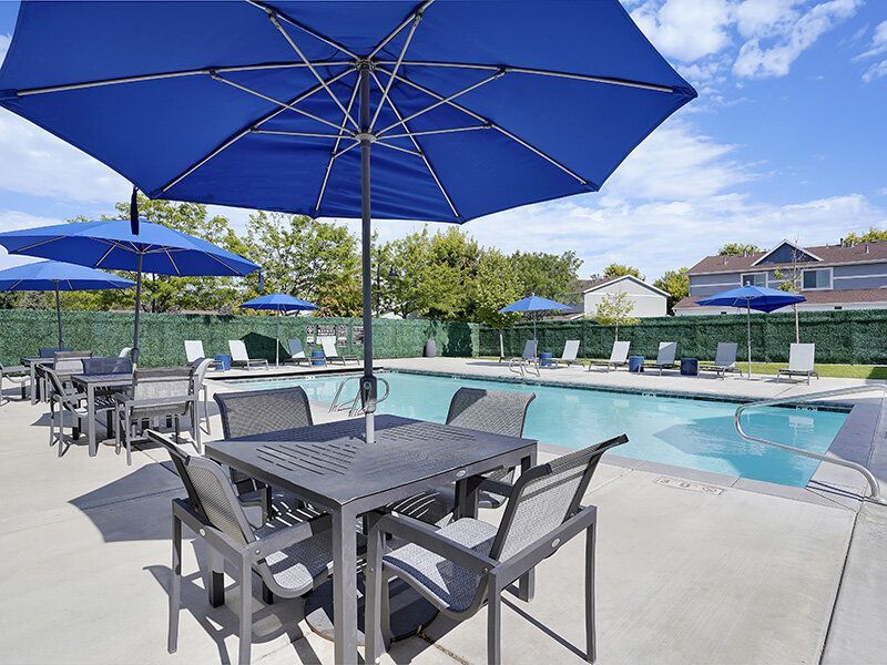 Outdoor apartment pool area with blue tables, chairs, and umbrellas.