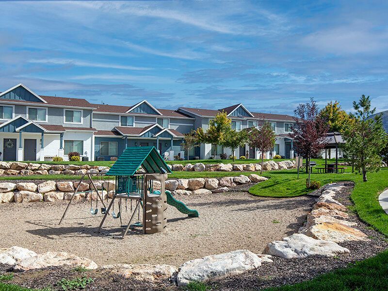 Playground with swings and a slide in a landscaped apartment community.