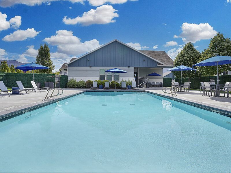 Outdoor pool area at a multifamily community with lounge chairs and blue umbrellas.