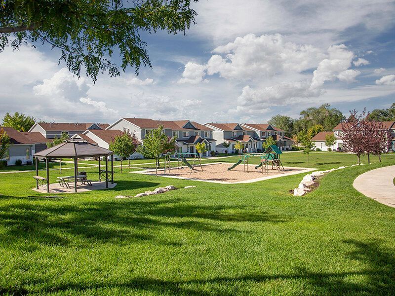 A sunny apartment community lawn with a playground, gazebo, and walking path.