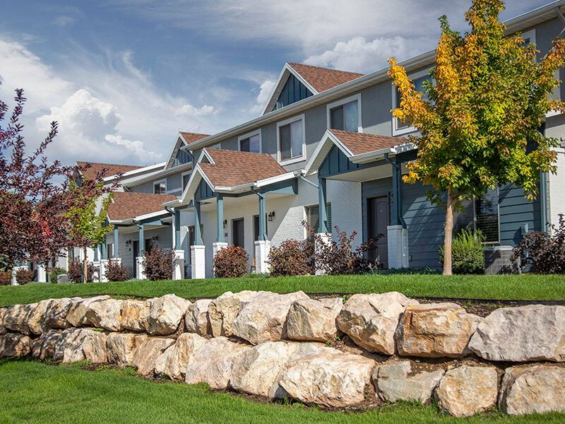 Exterior view of blue townhouse-style apartment buildings with gabled roofs and landscaped front yards.
