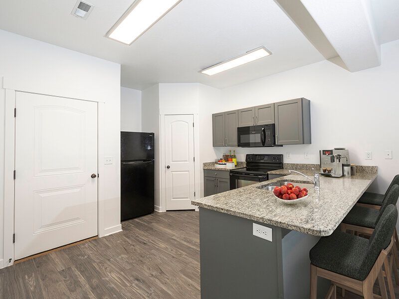 Open kitchen with granite island, gray cabinets, and stainless-steel appliances.