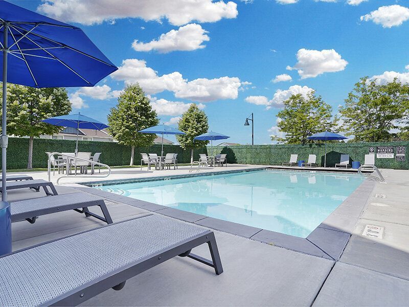 Outdoor pool area with lounge chairs, blue umbrellas, and a clear blue sky.