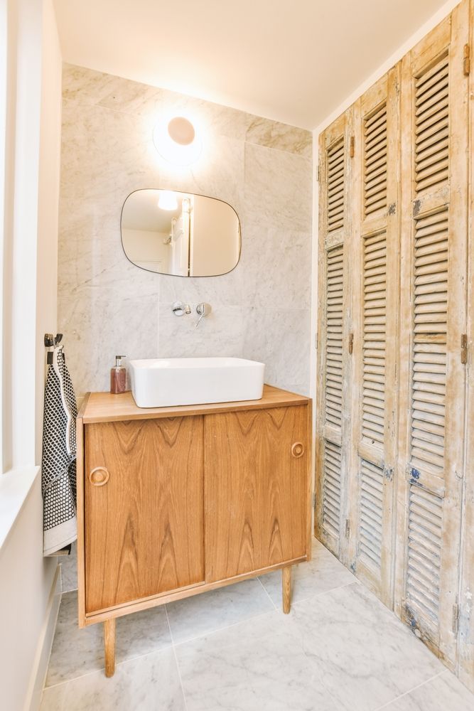 Bathroom with wooden cabinet, white sink, decorative mirror, and shutter doors.